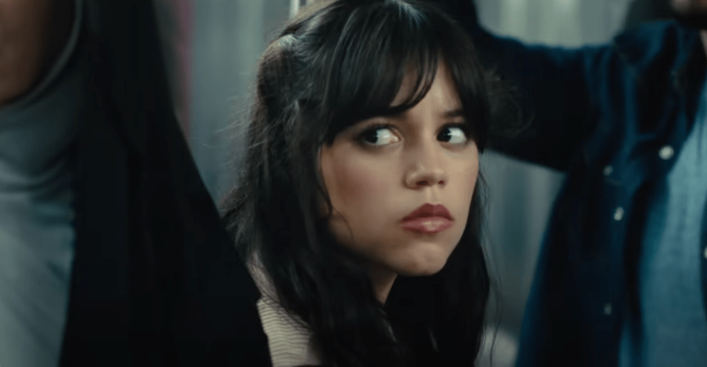 Una foto de la próxima película Scream 6 muestra a la actriz Jenny Ortega con cabello largo y oscuro sentada en un tren subterráneo luciendo preocupada.