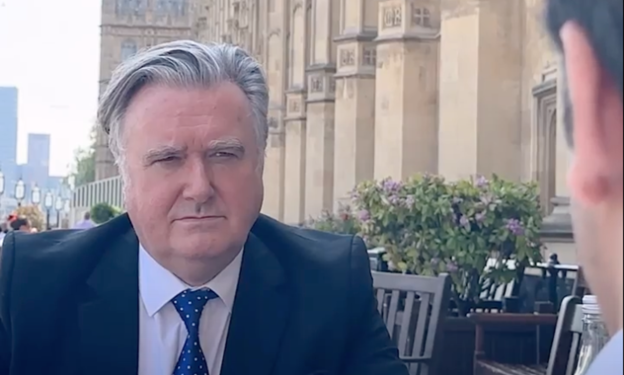 John Nicolson, a white man with grey hair, sitting outside the House of Commons