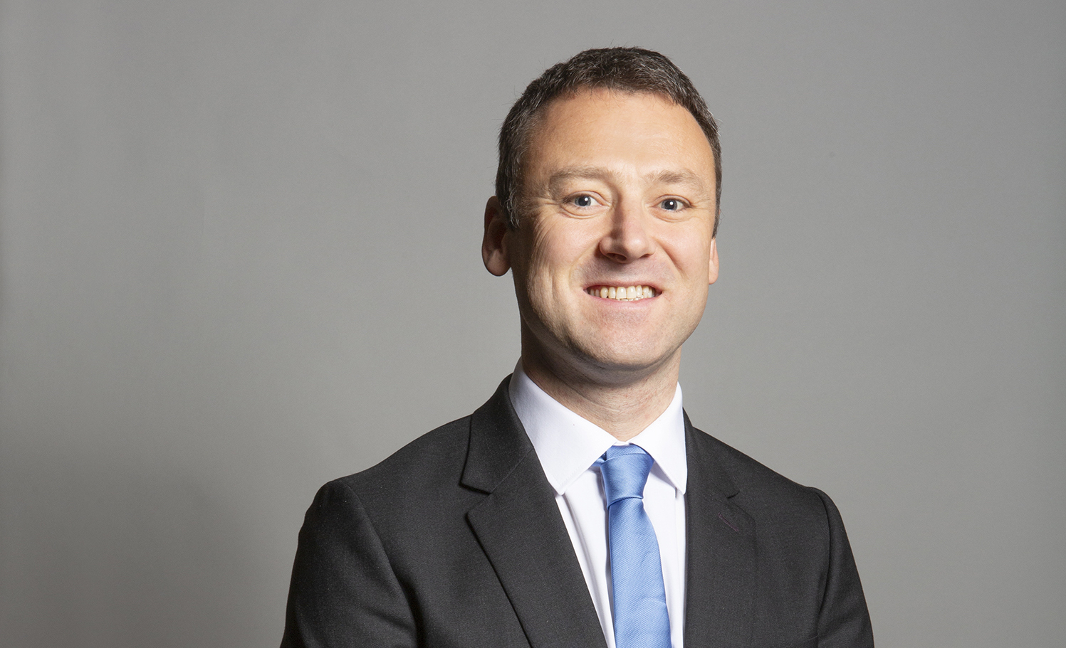 Conservative MP Brendan Clarke-Smith standing in a suit and blue tie against a grey background