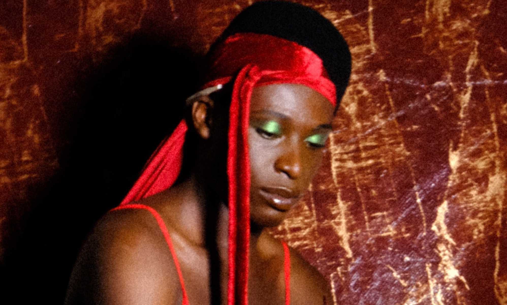 A character from Soft Bwoi - a Black man wearing a red durag and green eye shadow
