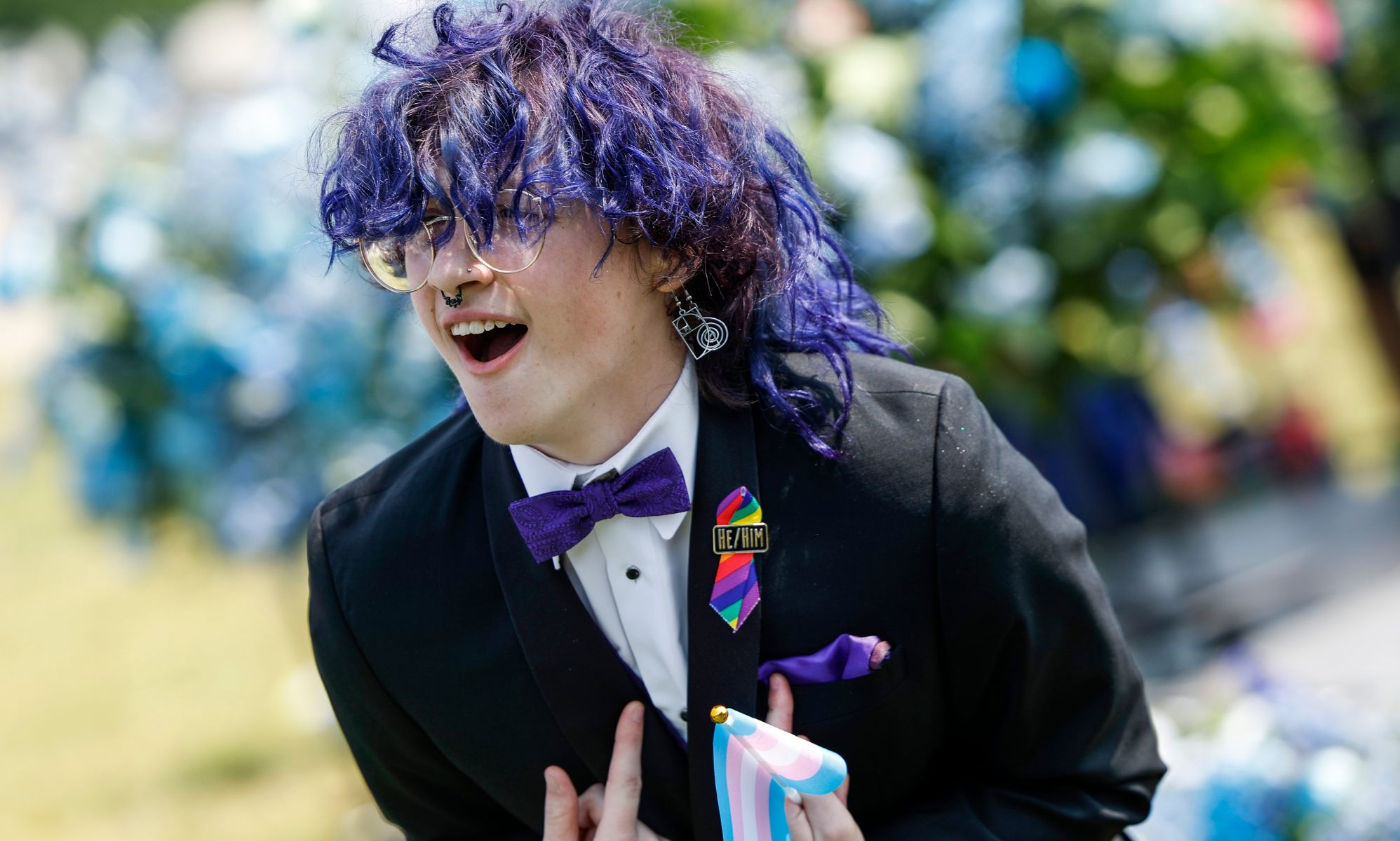 An Arkansas queer young person, wearing a suit and bow tie, leans over with their hands pointing inward.