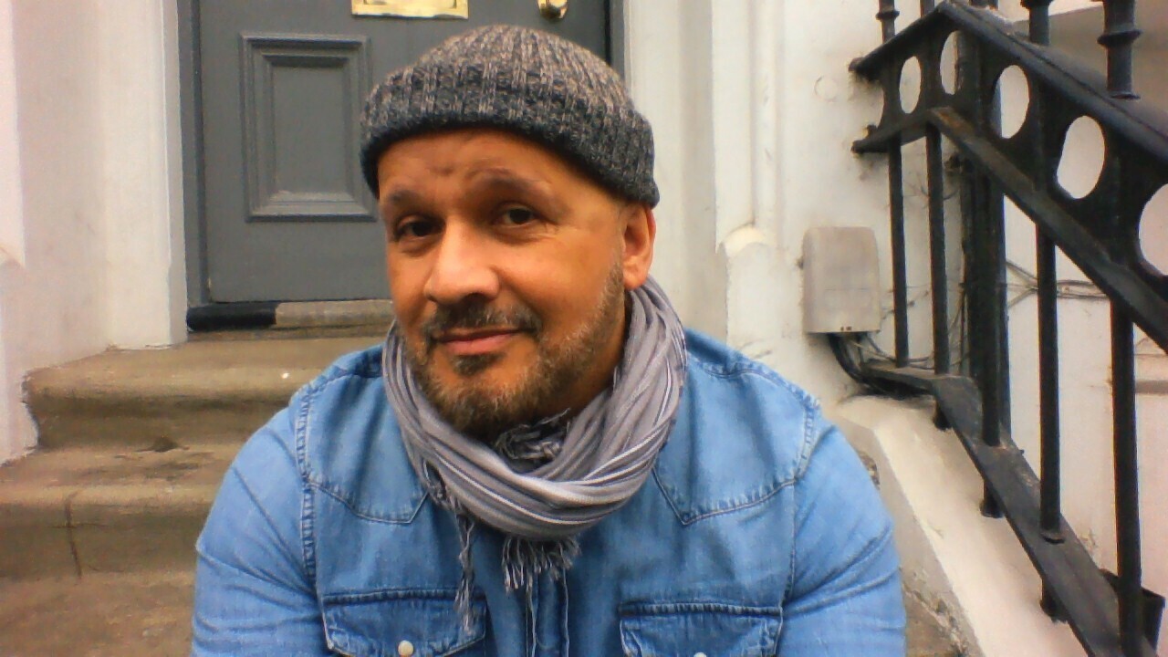 Paul, a mixed-race man with a greying beard, wearing a beanie hat, denim shirt and a scarf