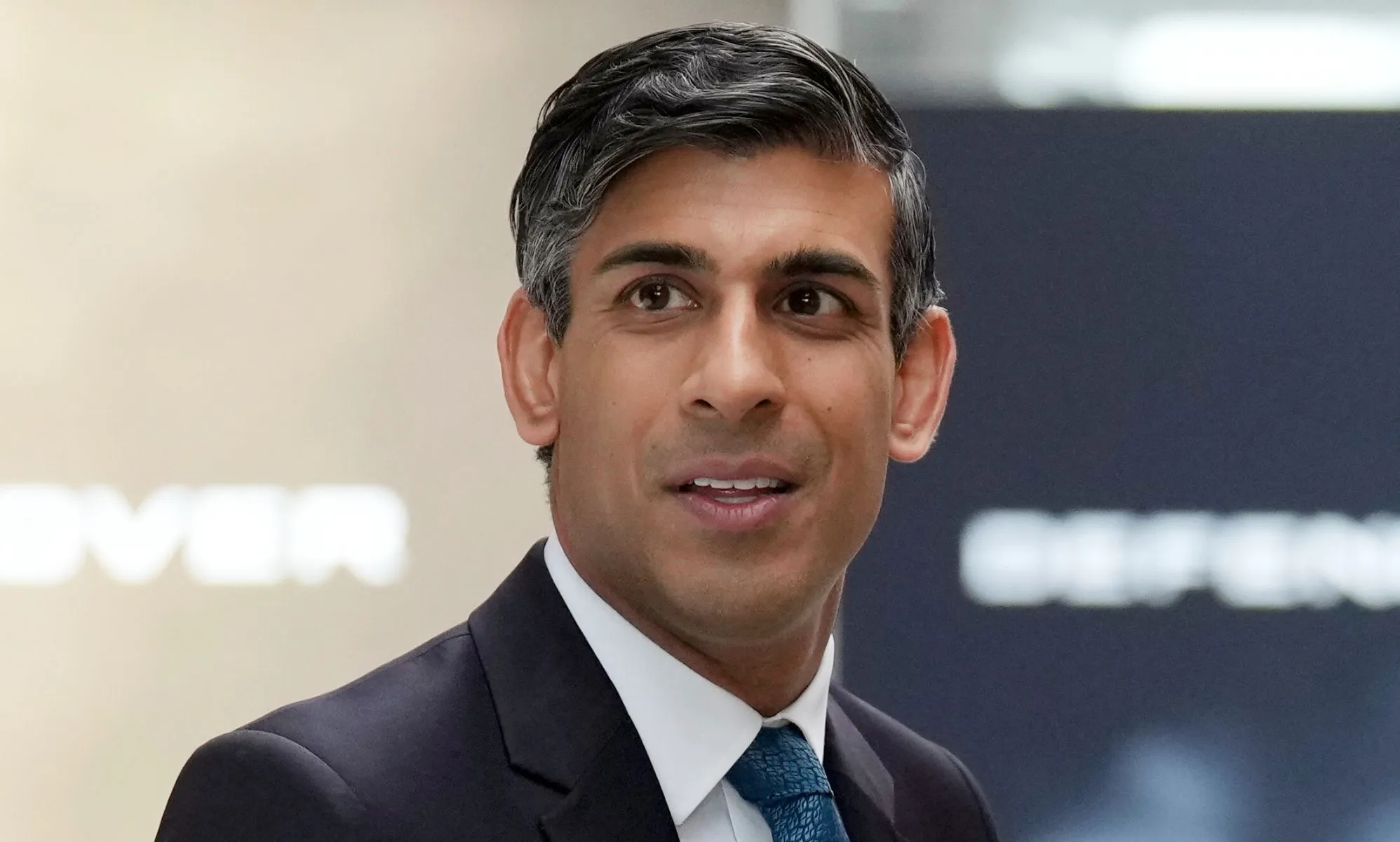 Rishi Sunak looking off into the distance, while wearing a suit and blue tie.