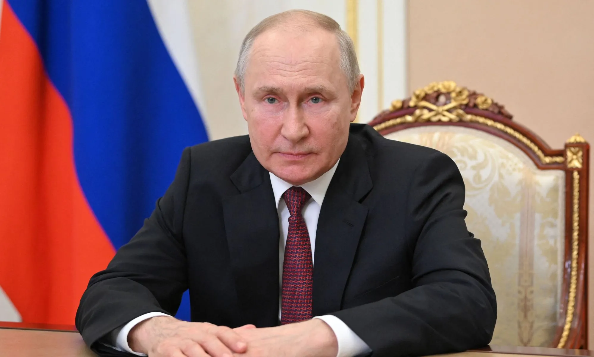 Russian president Vladimir Putin, who has frequently attacked LGBTQ+ and trans rights, wears a suit and tie as he sits at a desk