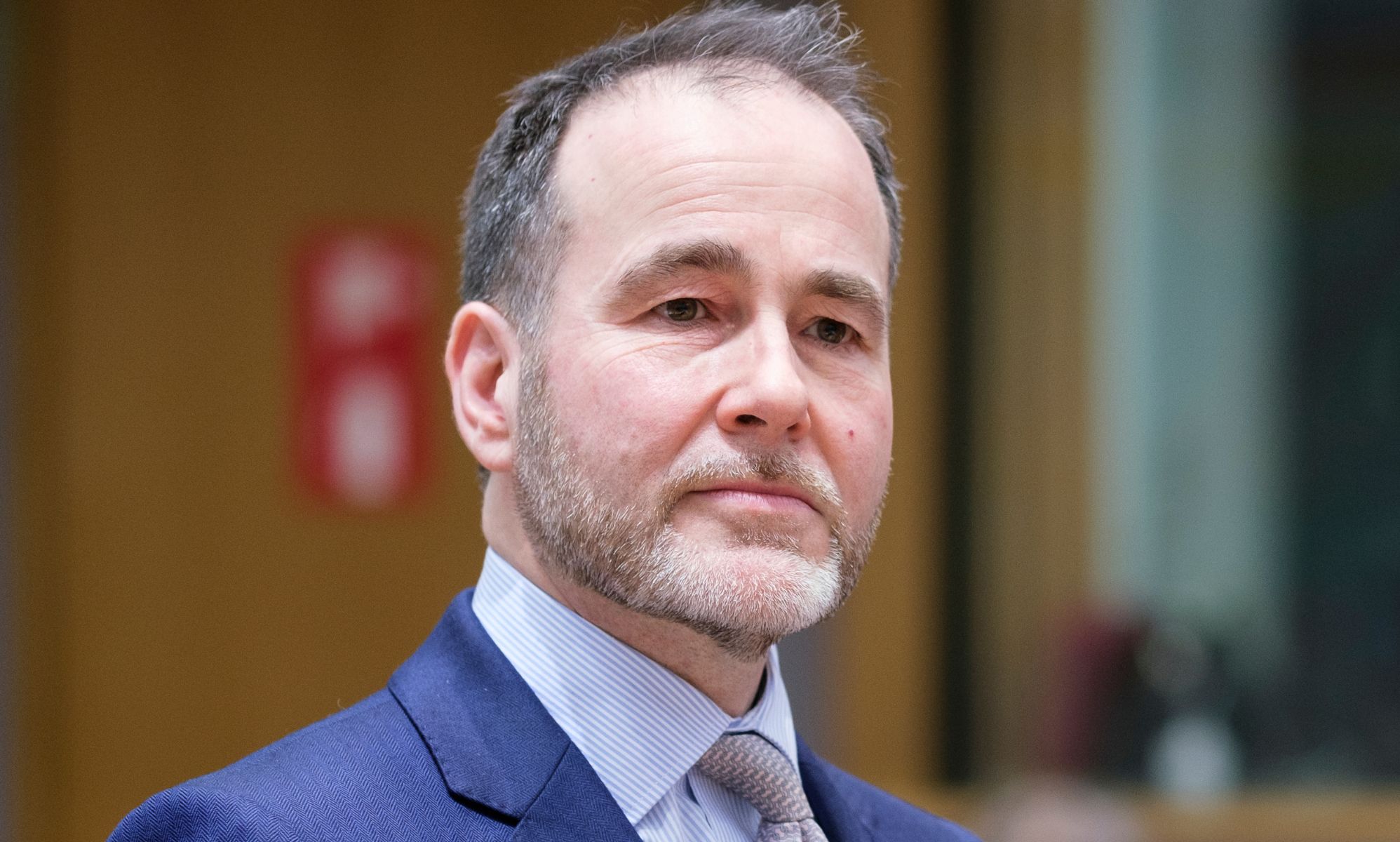 Chris Pincher, wearing a blue suit and purple tie, looks off in the distance.