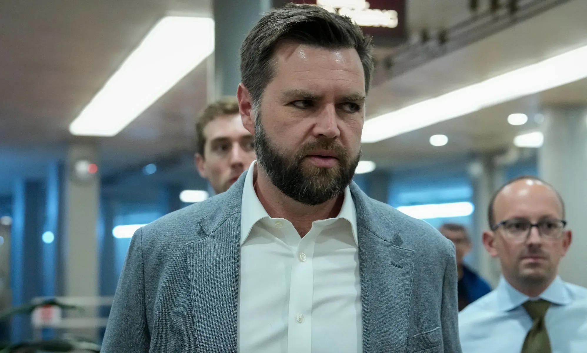 JD Vance, infront of several individuals, walks through an open room.