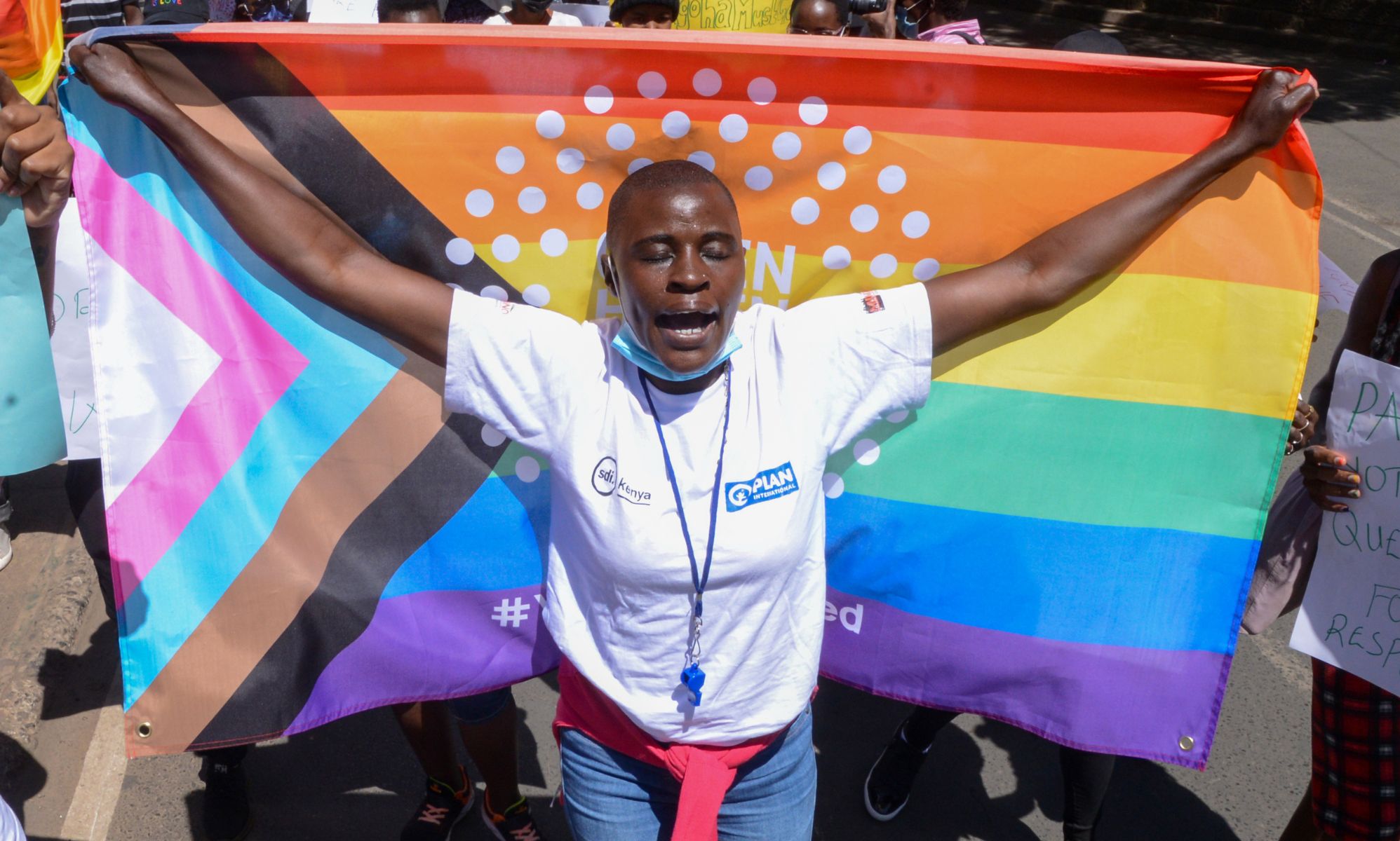 A Kenya LGBTQ+ activist holds up a Progress Pride flag behind them.