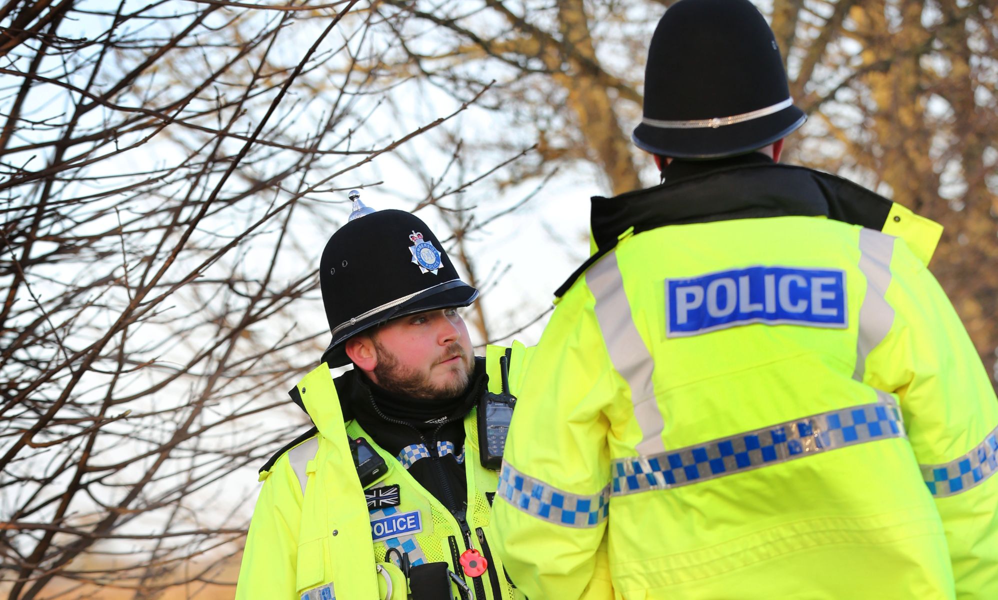 Two police officers wear the yellow, blue and black uniforms associated with law enforcement in England and Wales as they stand at the scene of a crime
