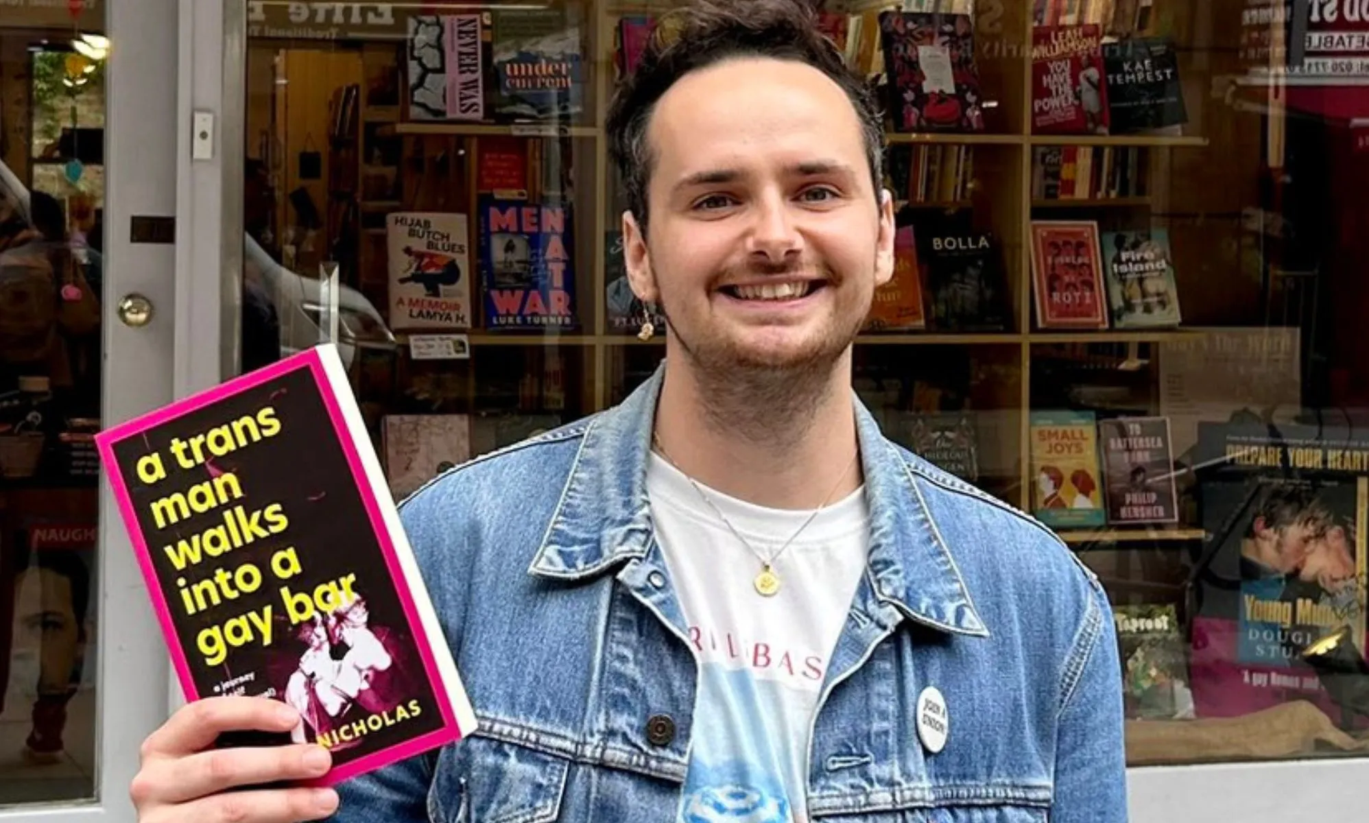 A picture of Harry Nicholas, in a denim jacket, holding a book that reads