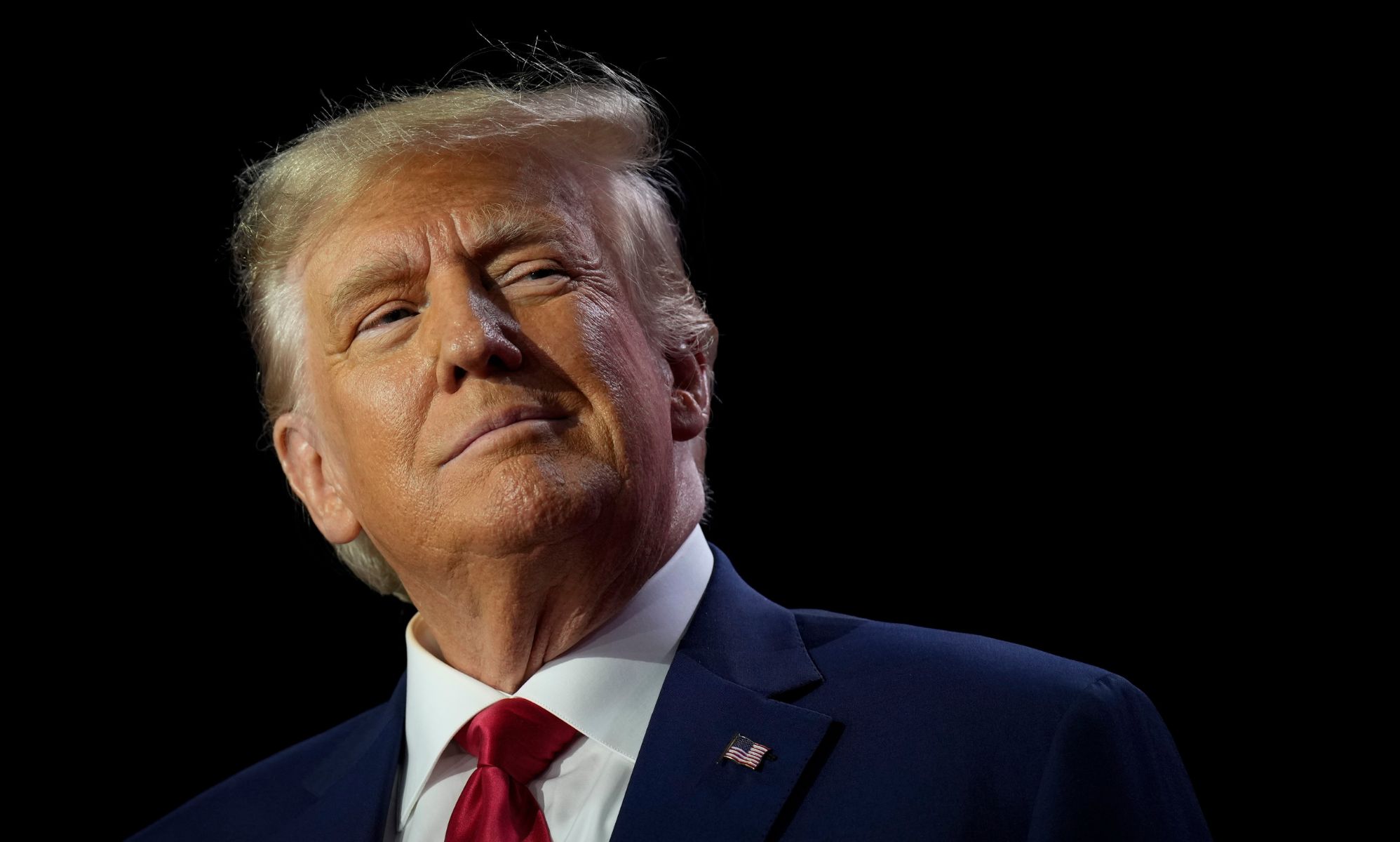 Donald Trump wears a white shirt, red tie and blue jacket as he stares somewhere off camera