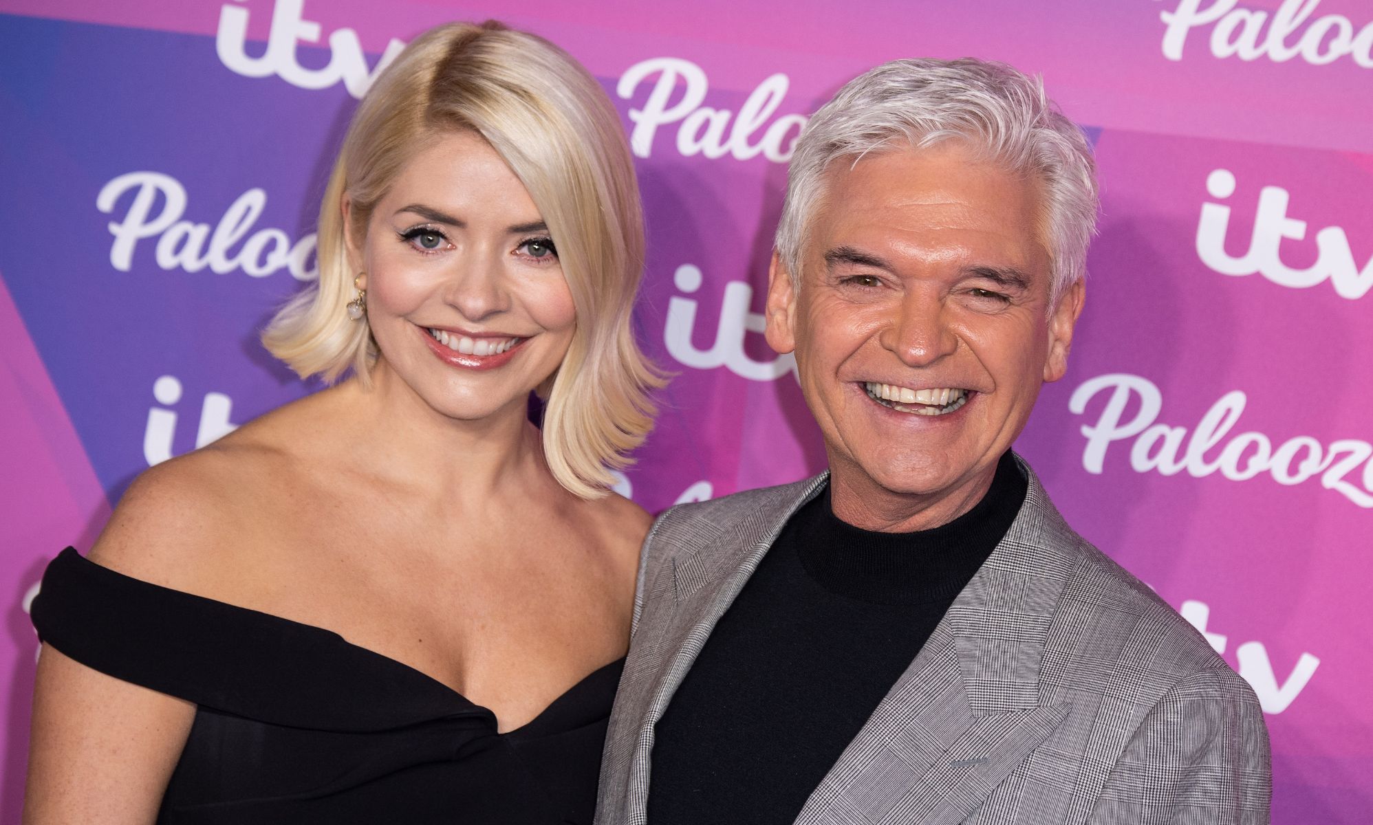 Holly Willoughby wears a black dress as she stands alongside Phillip Schofield in front of a purple background