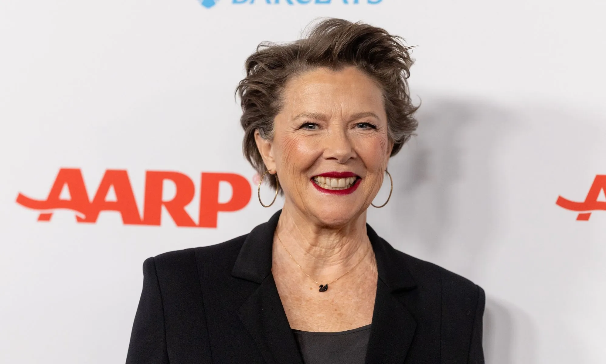 Annette Bening in a black blazer and top smiling at the camera while on the red carpet.