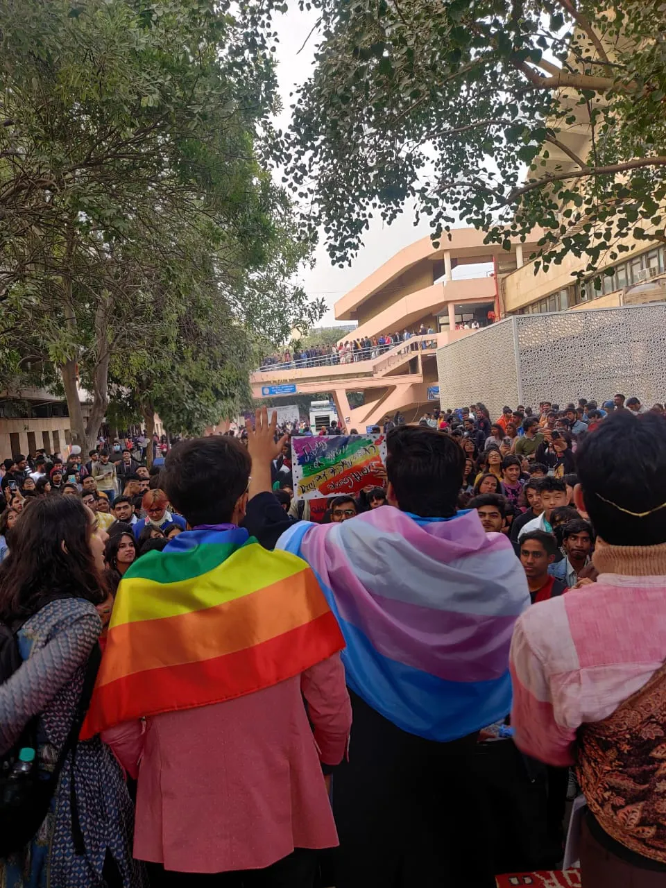 A group of Indian marchers at a Pride Parade, one draped in a transgender flag, the other in a pride flag.