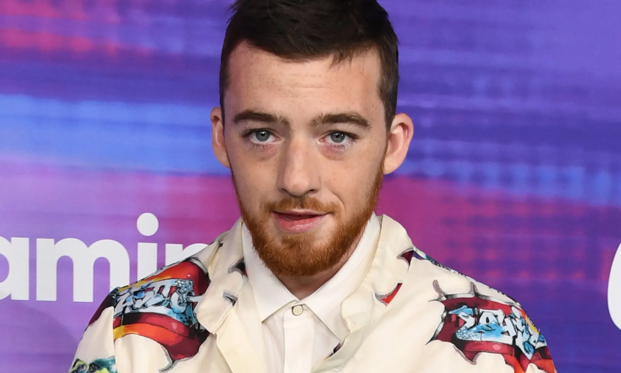 Angus Cloud, during a red carpet event, wears a white jacket with red graphics on it.