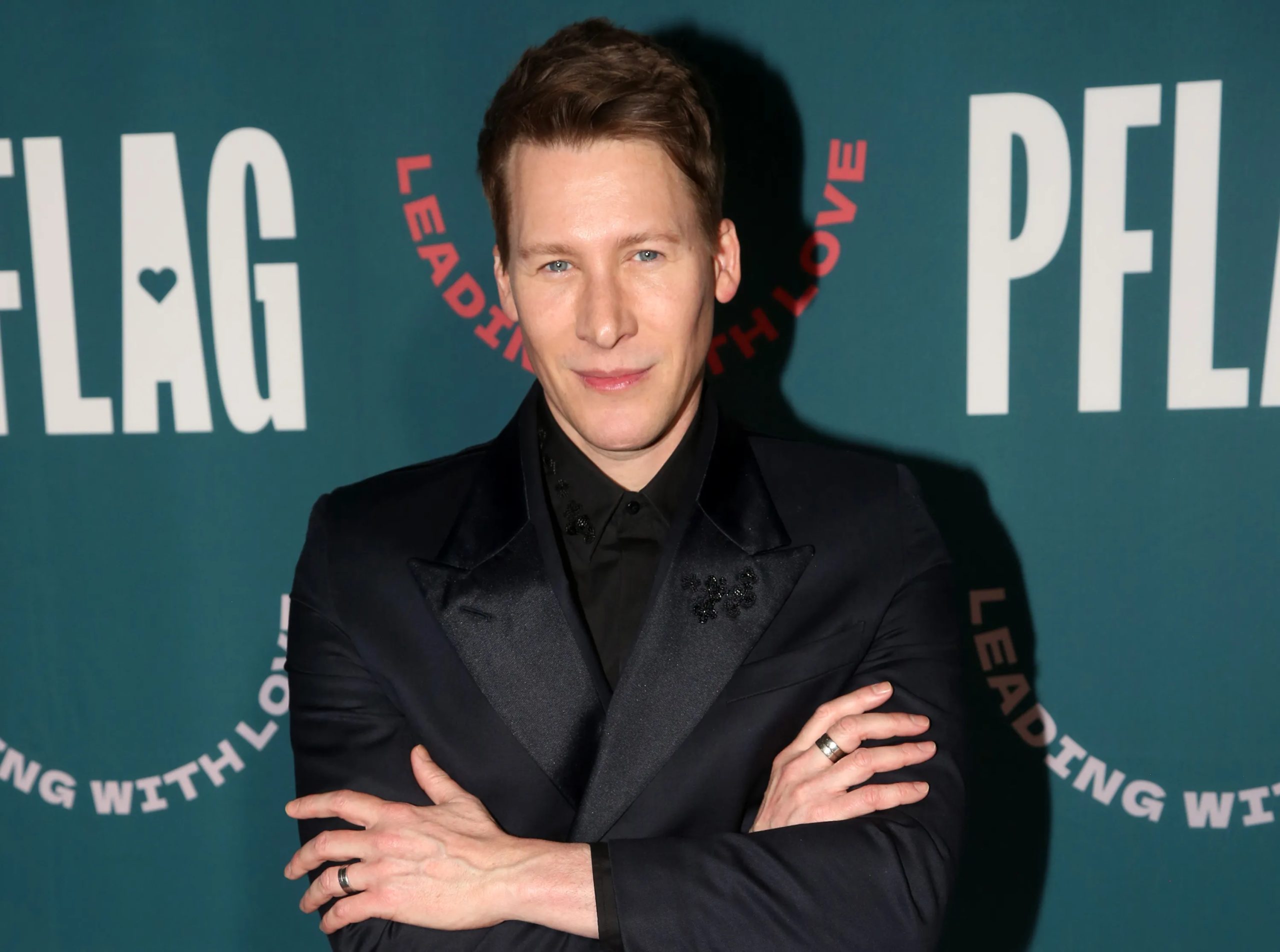 Dustin Lance Black poses on the red carpet in a black suit and shirt