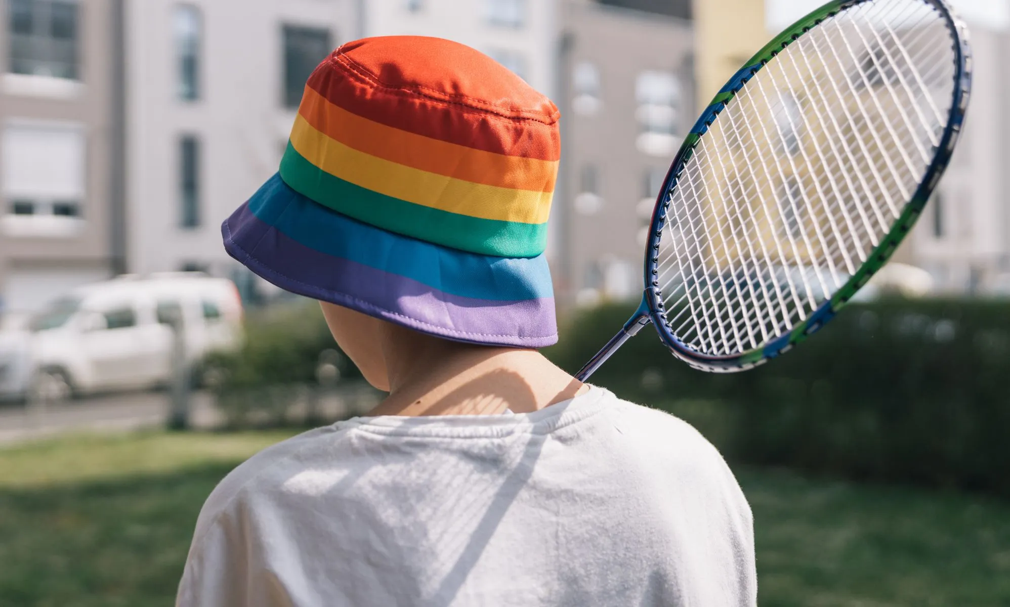 A person with a rainbow bucket hat holds a badminton racket.