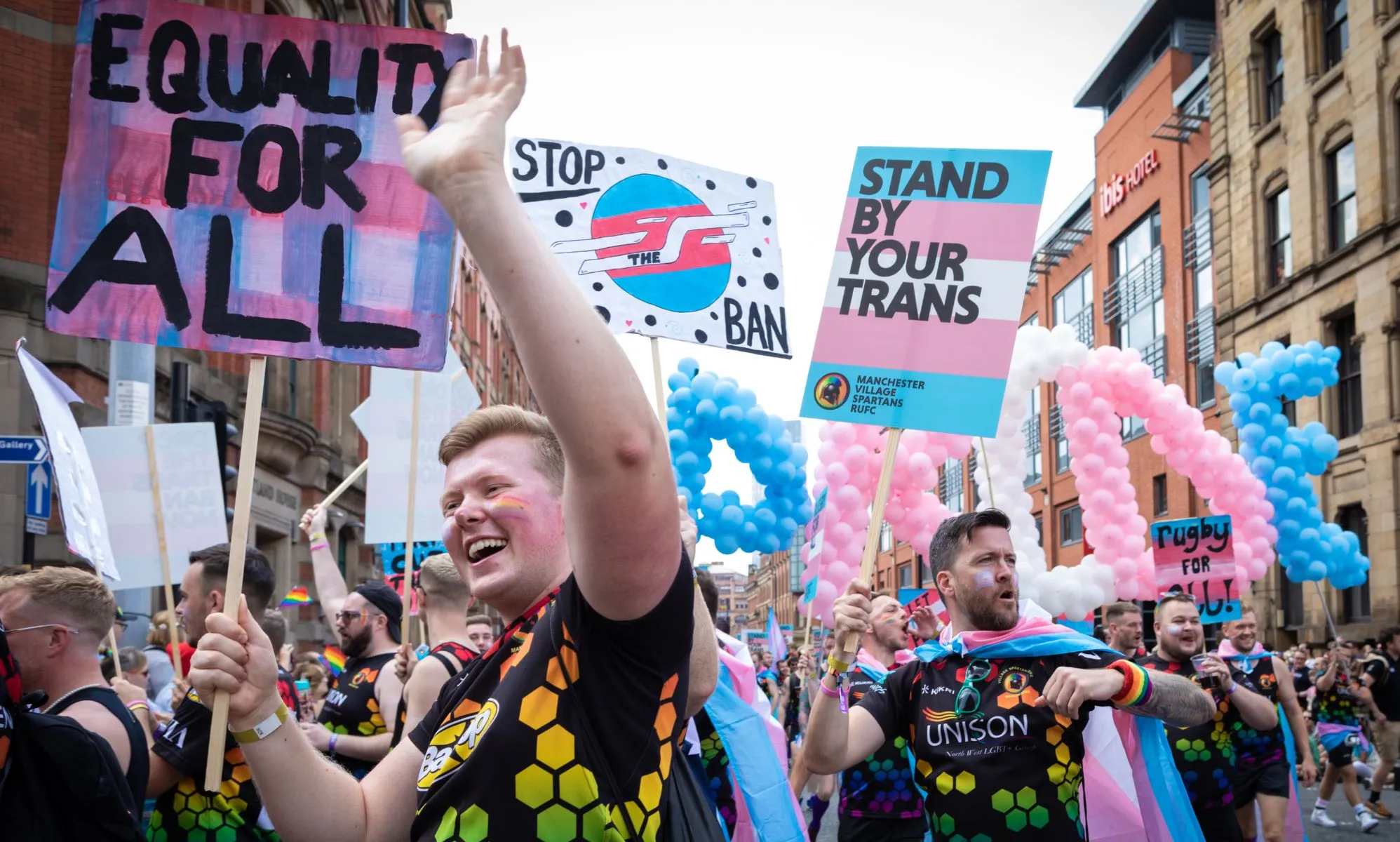 Pro-trans activists march side by side holding up signs of solidarity.