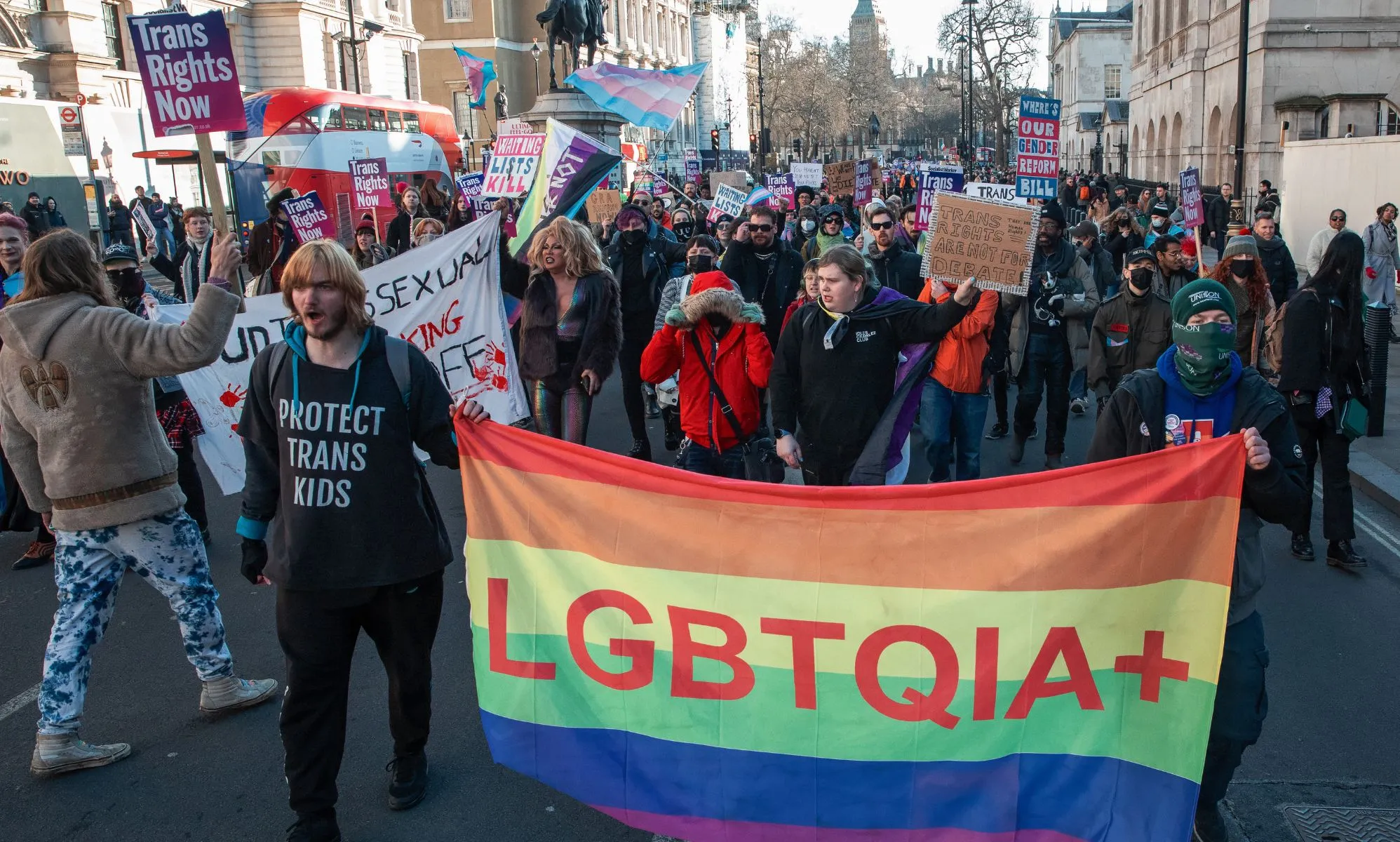 Protestors march through a street with pro-LGBTQ+ flags.