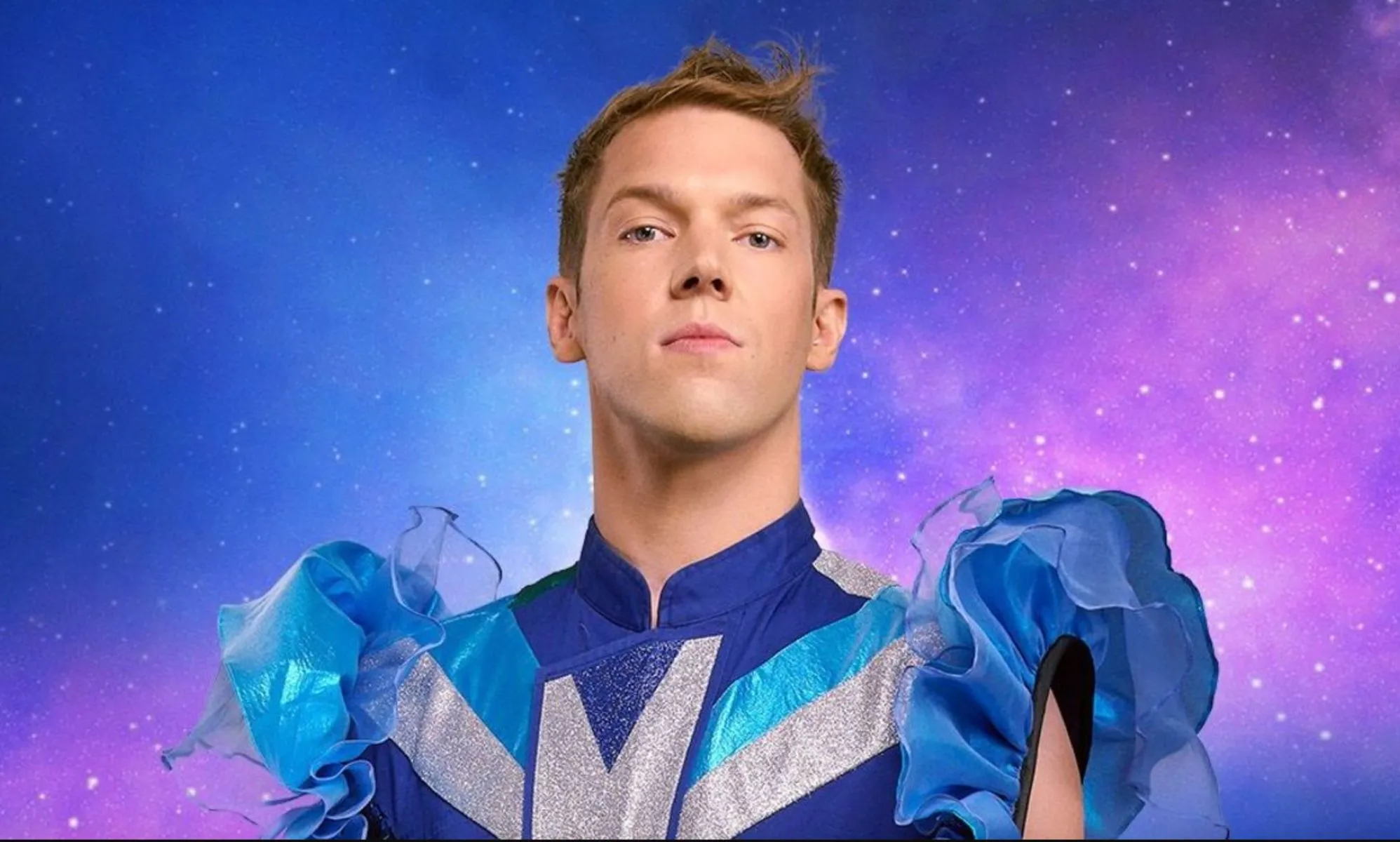 Drag Race Belgique judge Mustii in his promotional photo, wearing a blue and silver top with puffy blue sleeves.