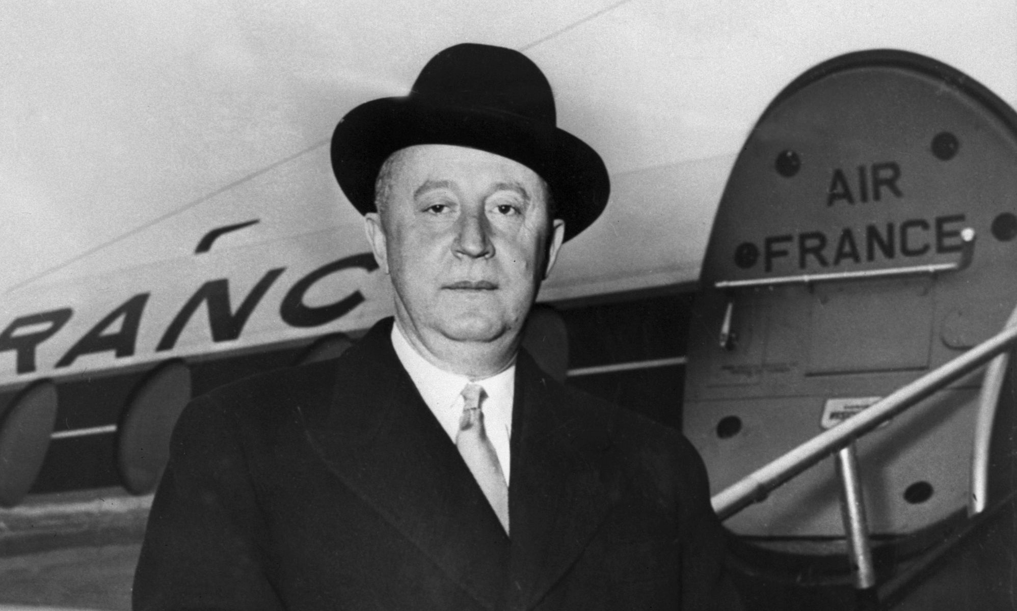 A black and white photo of fashion designer Christian Dior stood in front of an Air France plane.