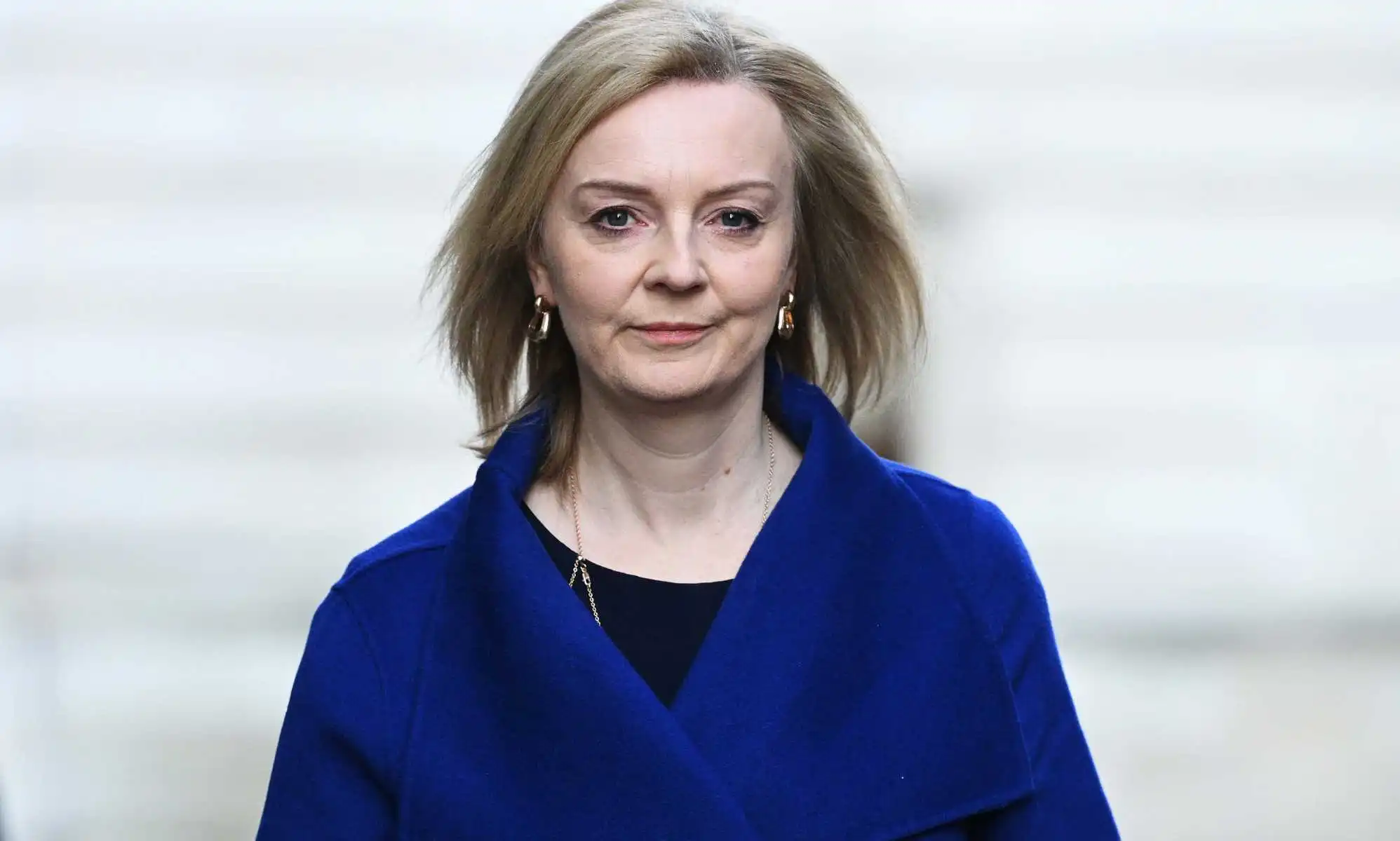 Liz Truss pictured walking outdoors wearing a blue jacket.