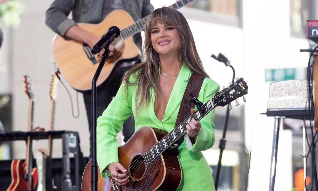 Maren Morris in a green suit playing the guitar.