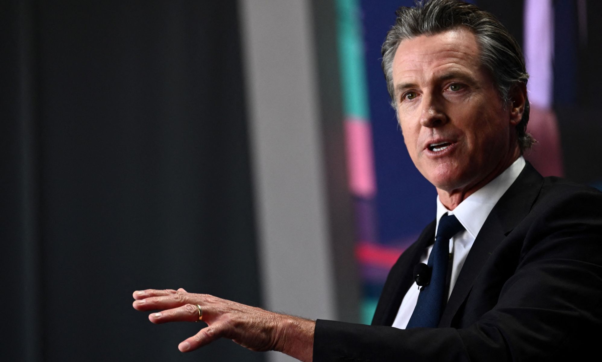 California governor Gavin Newsom wears a suit and tie as he gestures off screen.