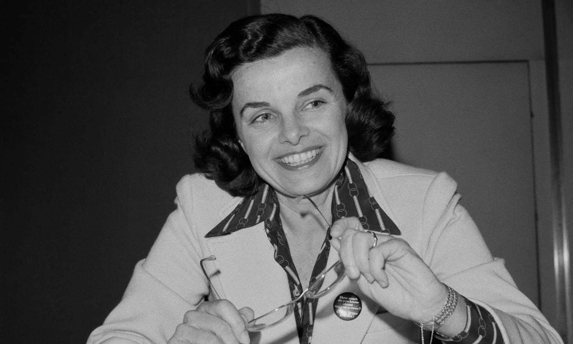 A black and white picture of Dianne Feinstein smiling as she holds a pair of glasses.