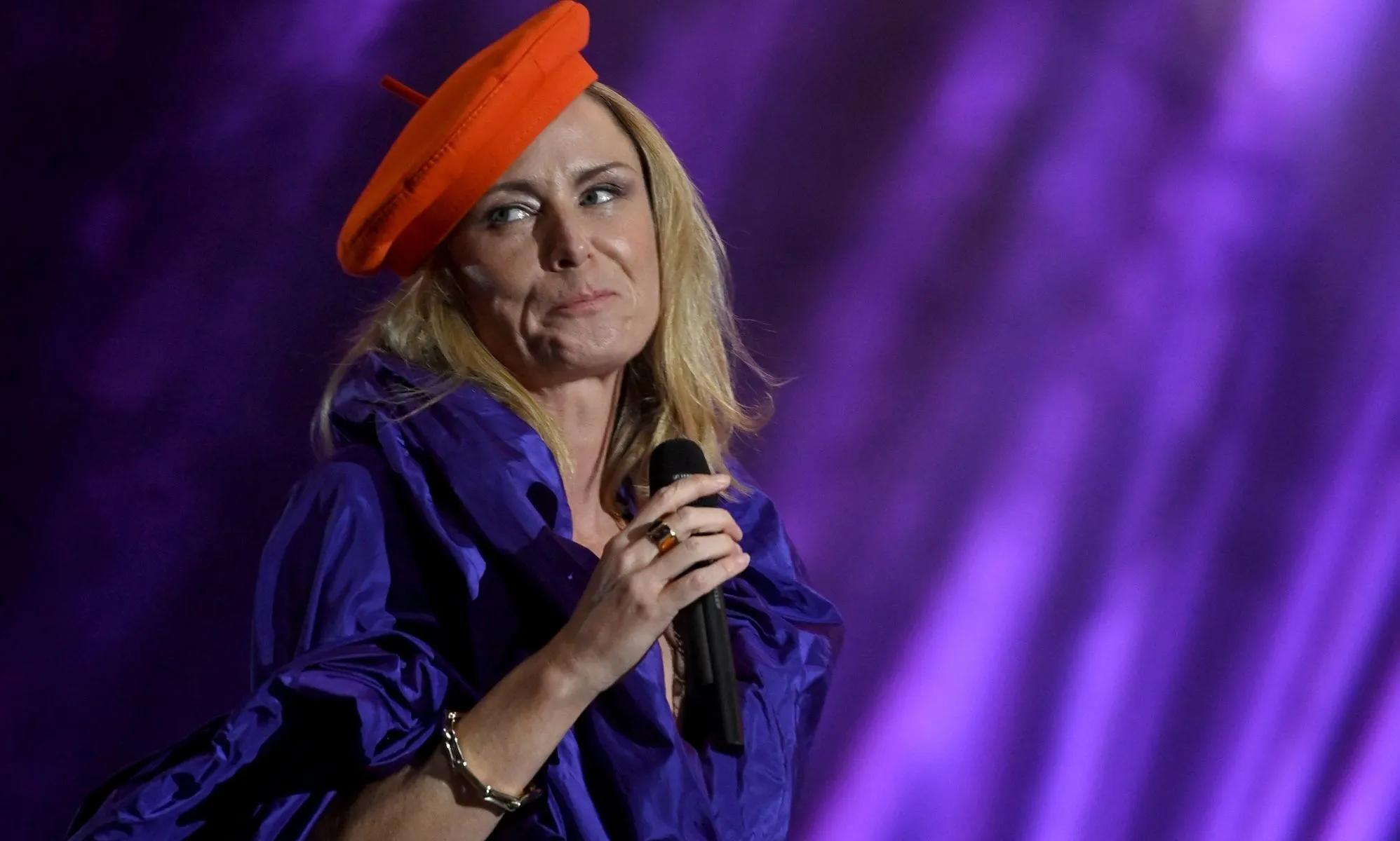 Singer-songwriter Róisín Murphy holds a microphone as she performs onstage in a purple outfit and with a red hat