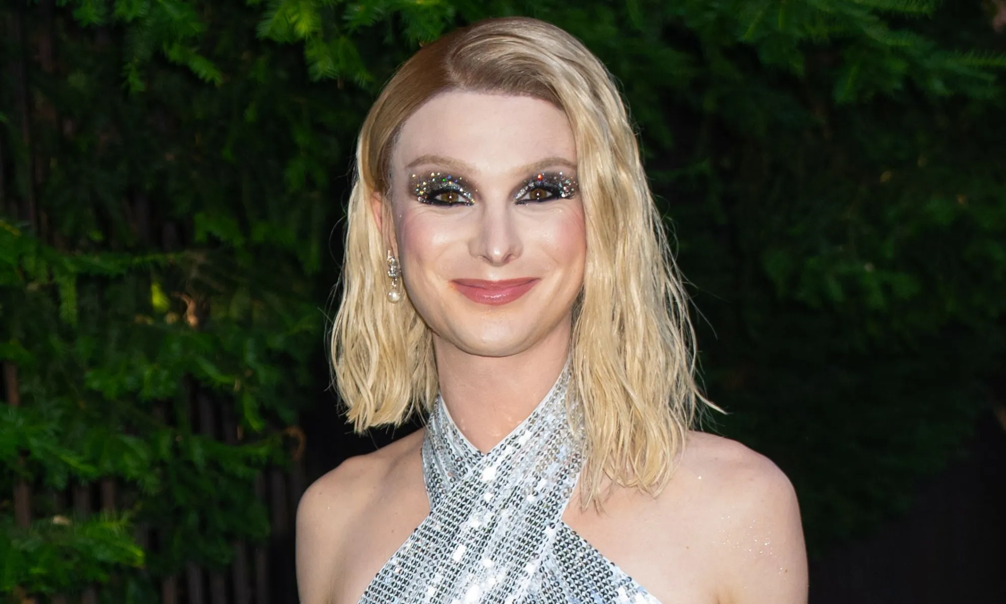 Dylan Mulvaney, in a silver dress, walking down a street.