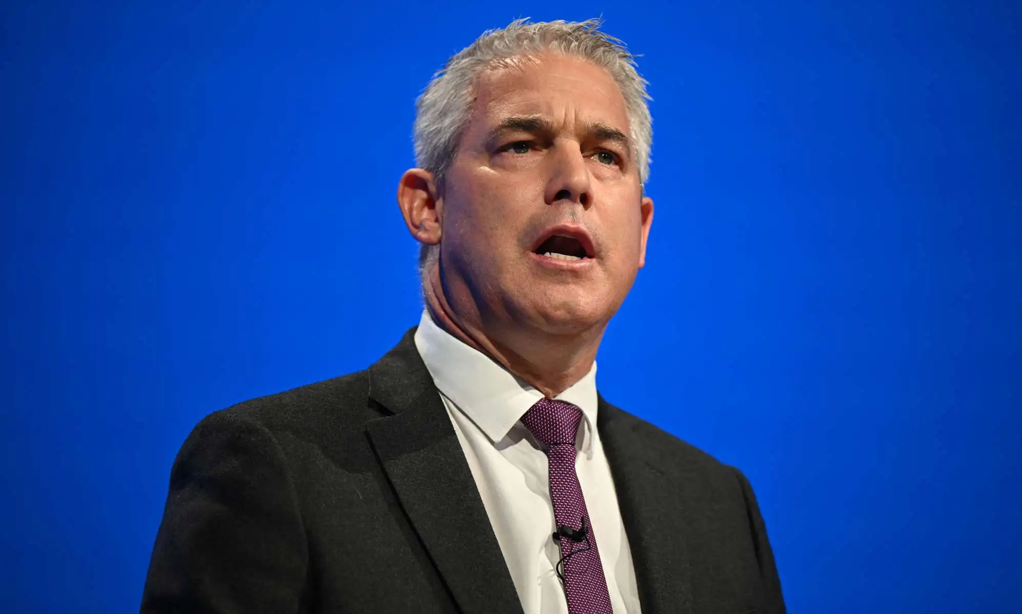 Steve Barclay giving a speech at the Conservative party conference in Manchester in October 2023. He is pictured wearing a dark suit and tie against a blue background.