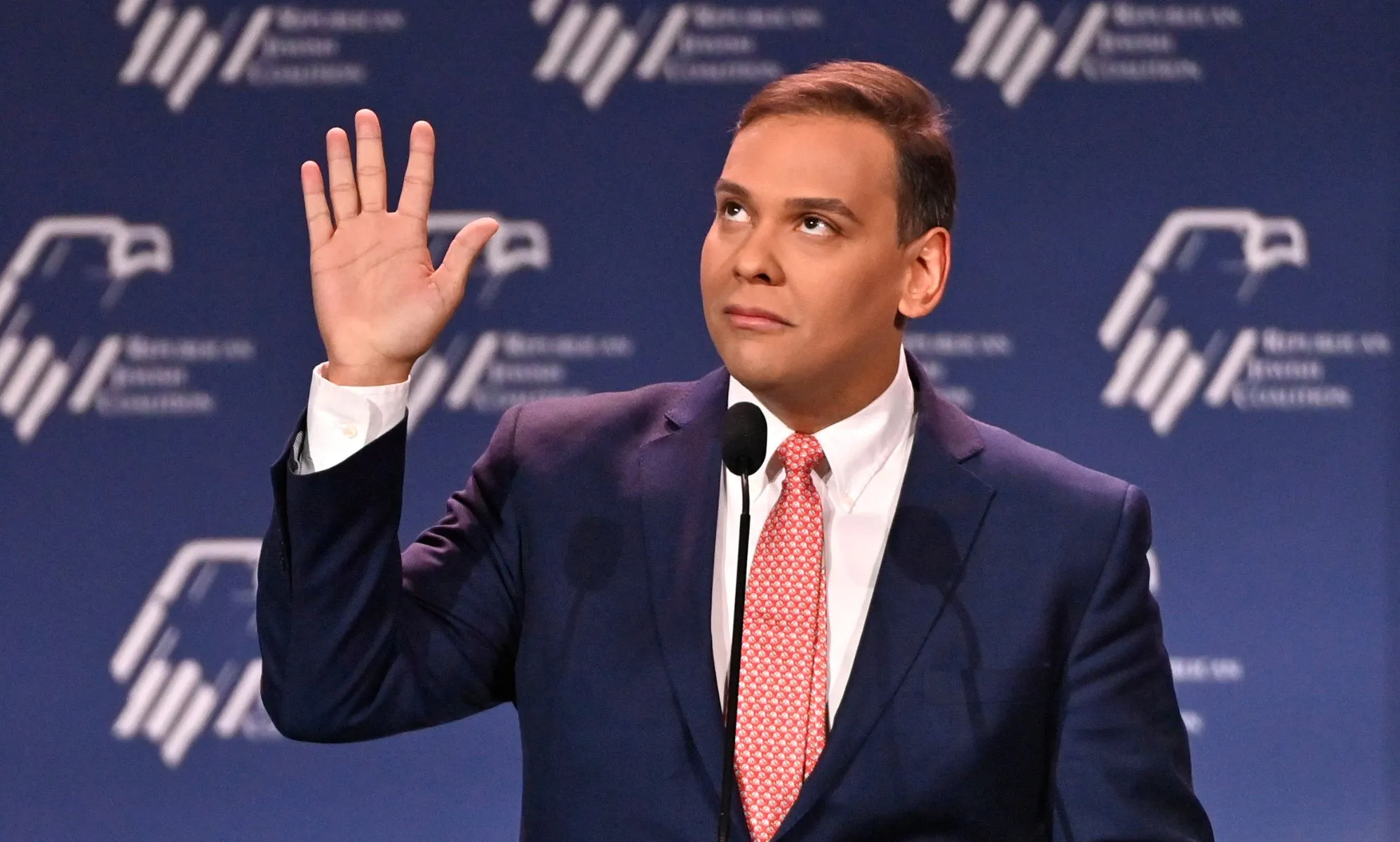 Republican politician George Santos gestures with his hands near his face while speaking at a podium