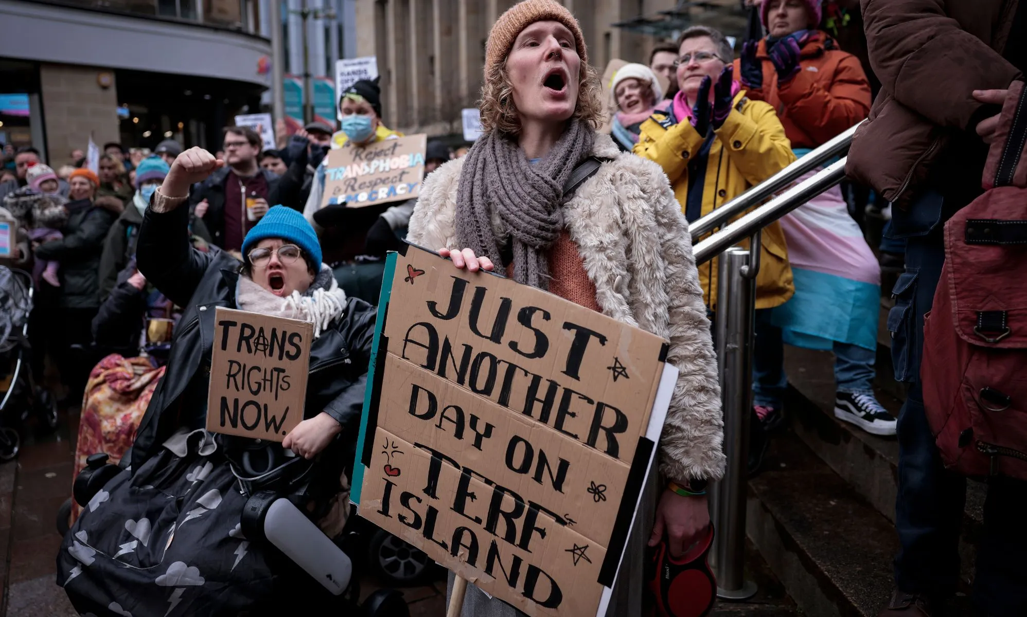 Protestors hold up signs reading