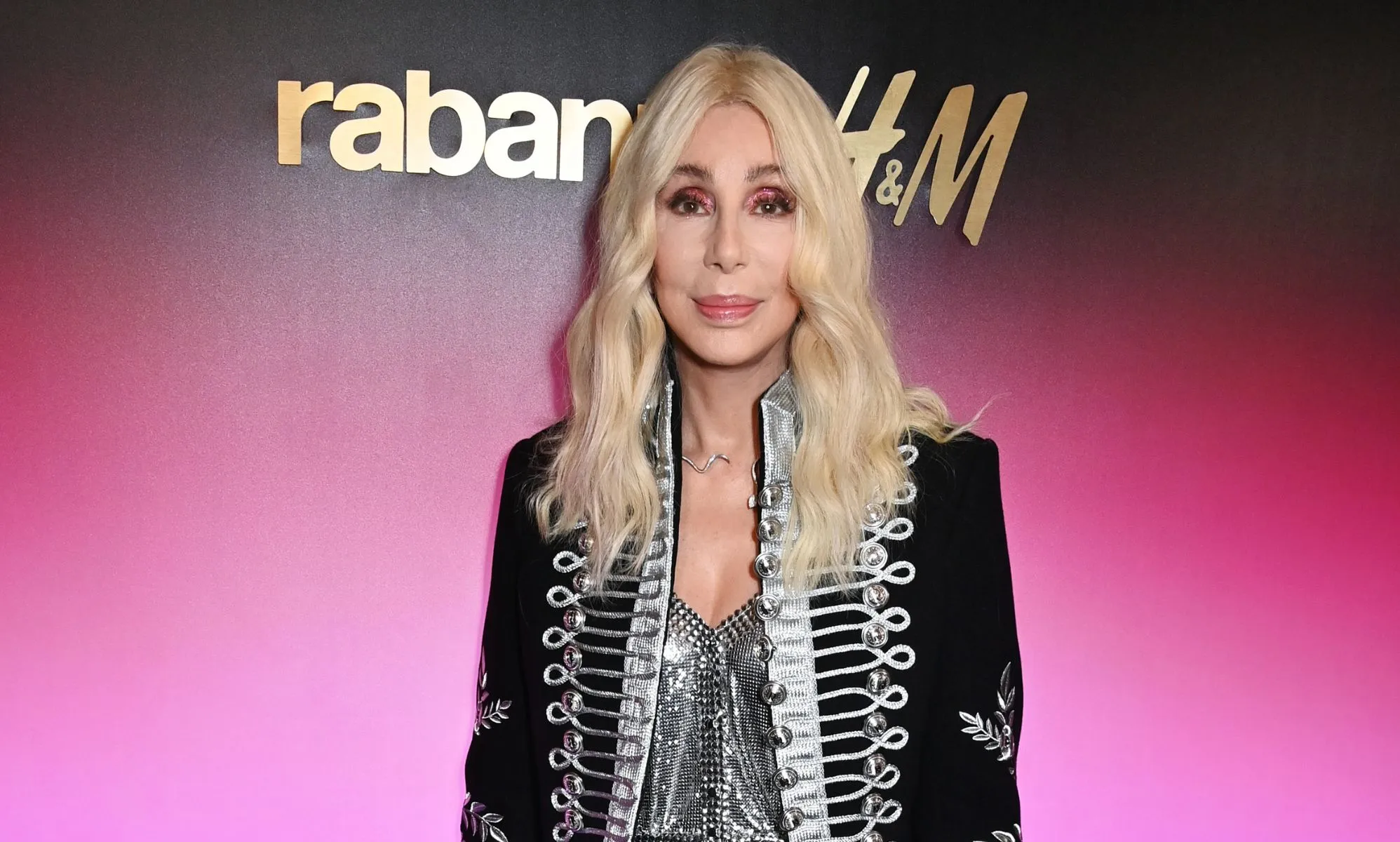 Pop singer Cher wears a silver corset type top with a silver, grey and black jacket and long blonde hair