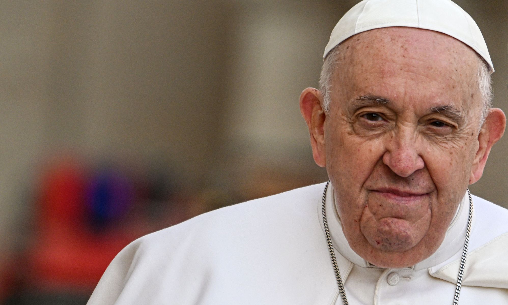 A close up photograph of Pope Francis, the leader of the Catholic Church, wearing white as he stares towards the camera