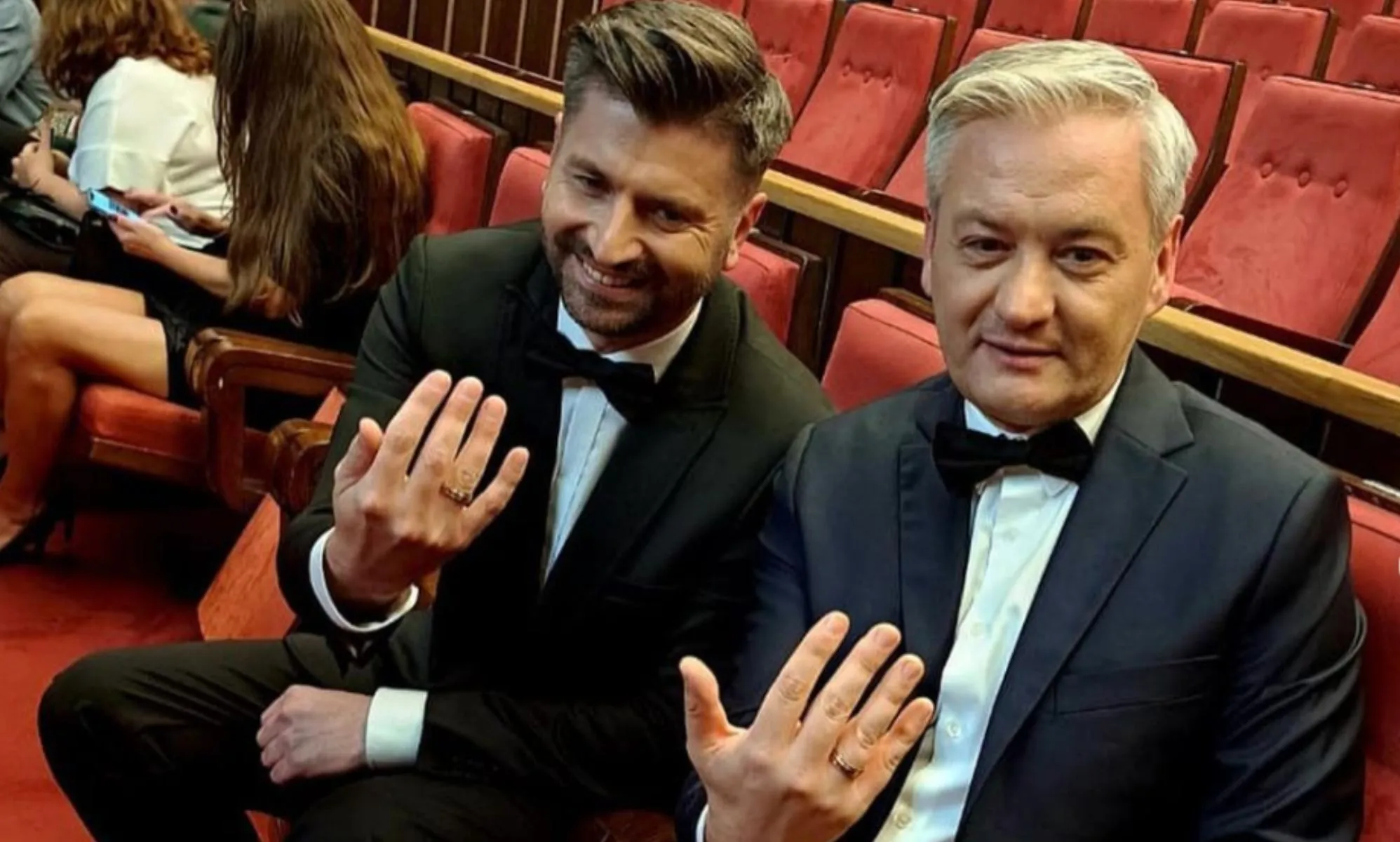 Polish politicians Robert Biedroń and Krzysztof Śmiszek sit on theatre chairs holding their hands out to show their wedding rings