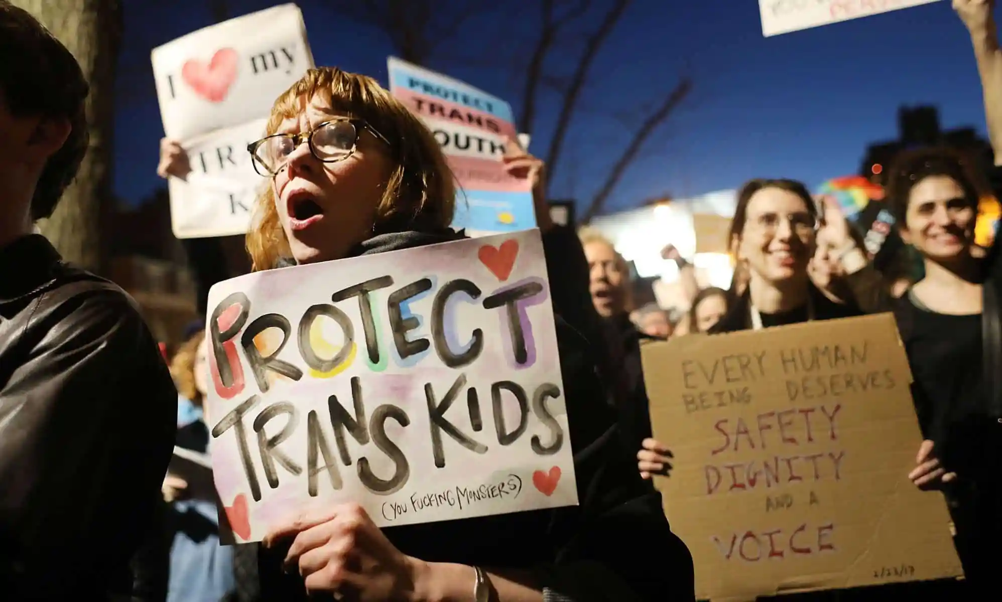 A person in gather amid a crowd in a protest holding a sign that reads
