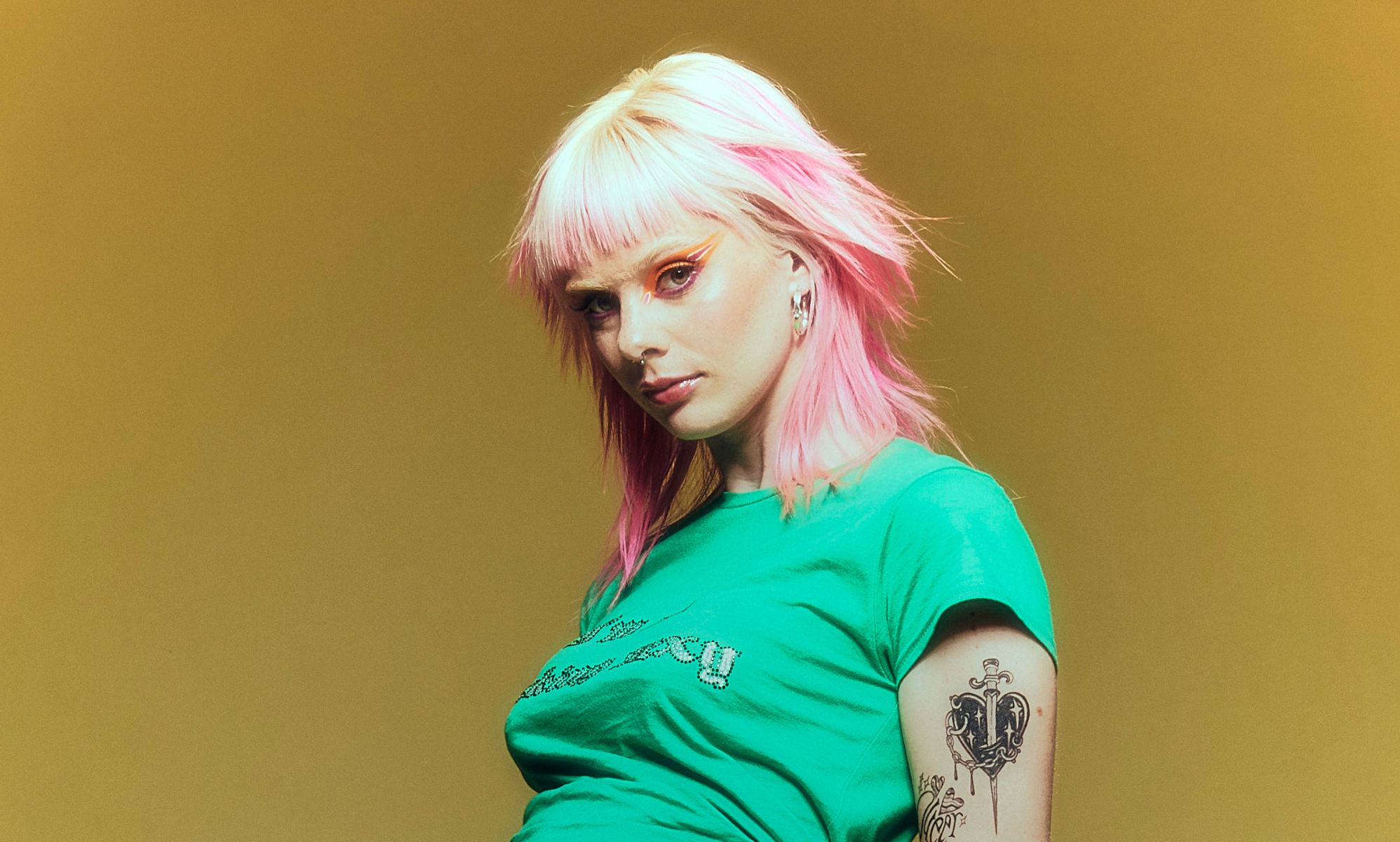 Pop singer Girli in a green top standing against a yellow background.