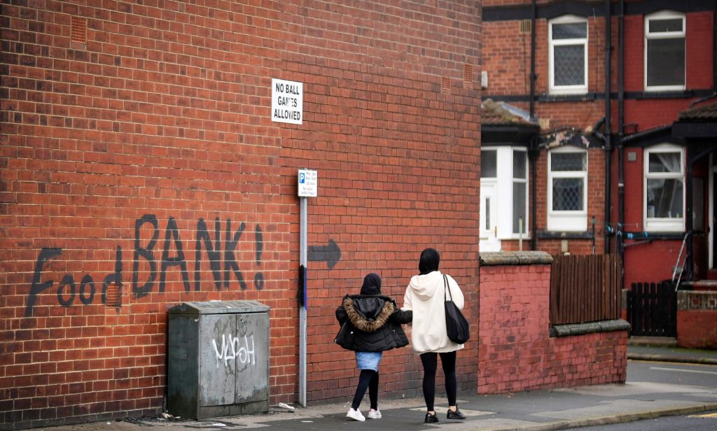 A mother and child can be seen walking past a food bank sign.