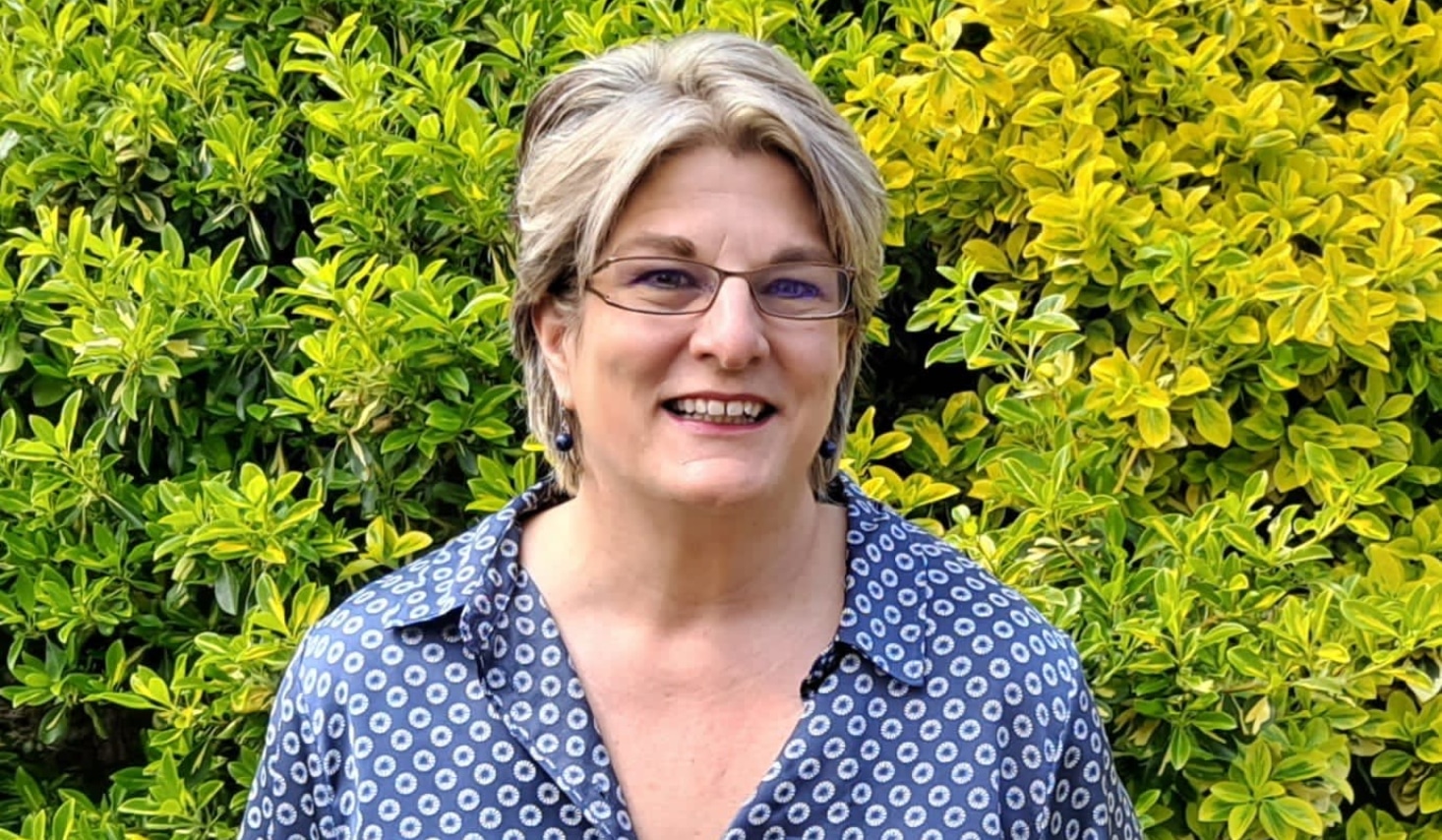 Jayne Ozanne smiling in front of some bushes