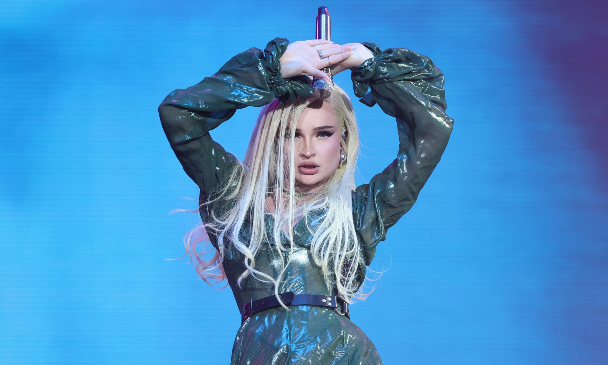 Kim Petras wears a sparkly outfit onstage as she holds a microphone above her head