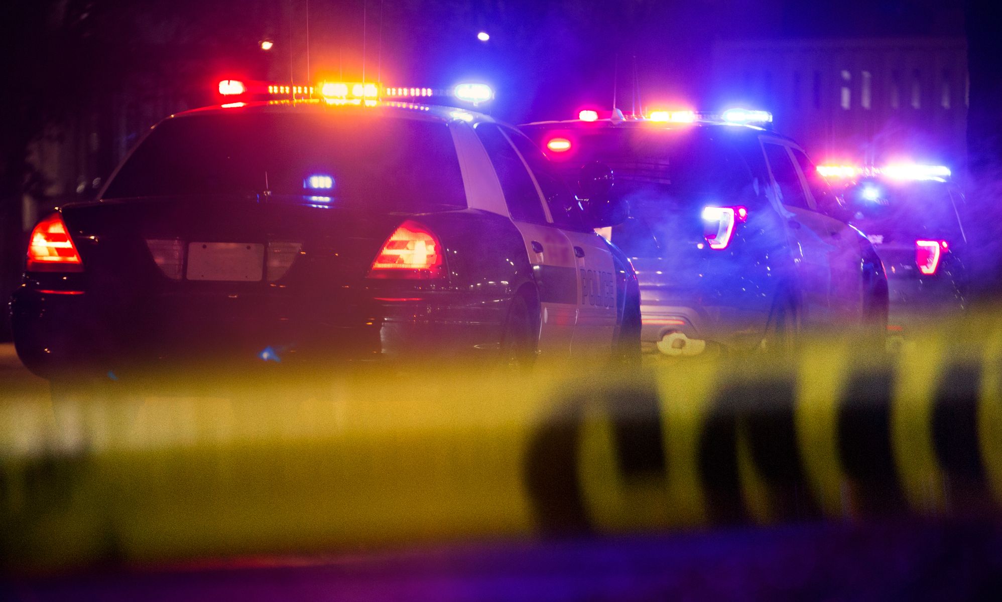 Two police cars driving away from police tape.