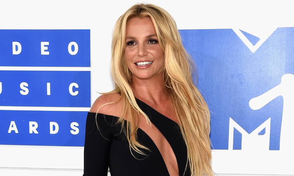 Britney Spears aparece con un vestido negro con recortes sobre un fondo azul y blanco