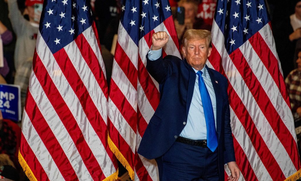 This picture shows Donald Trump standing against three American flags holding a raised fist to supporters.
