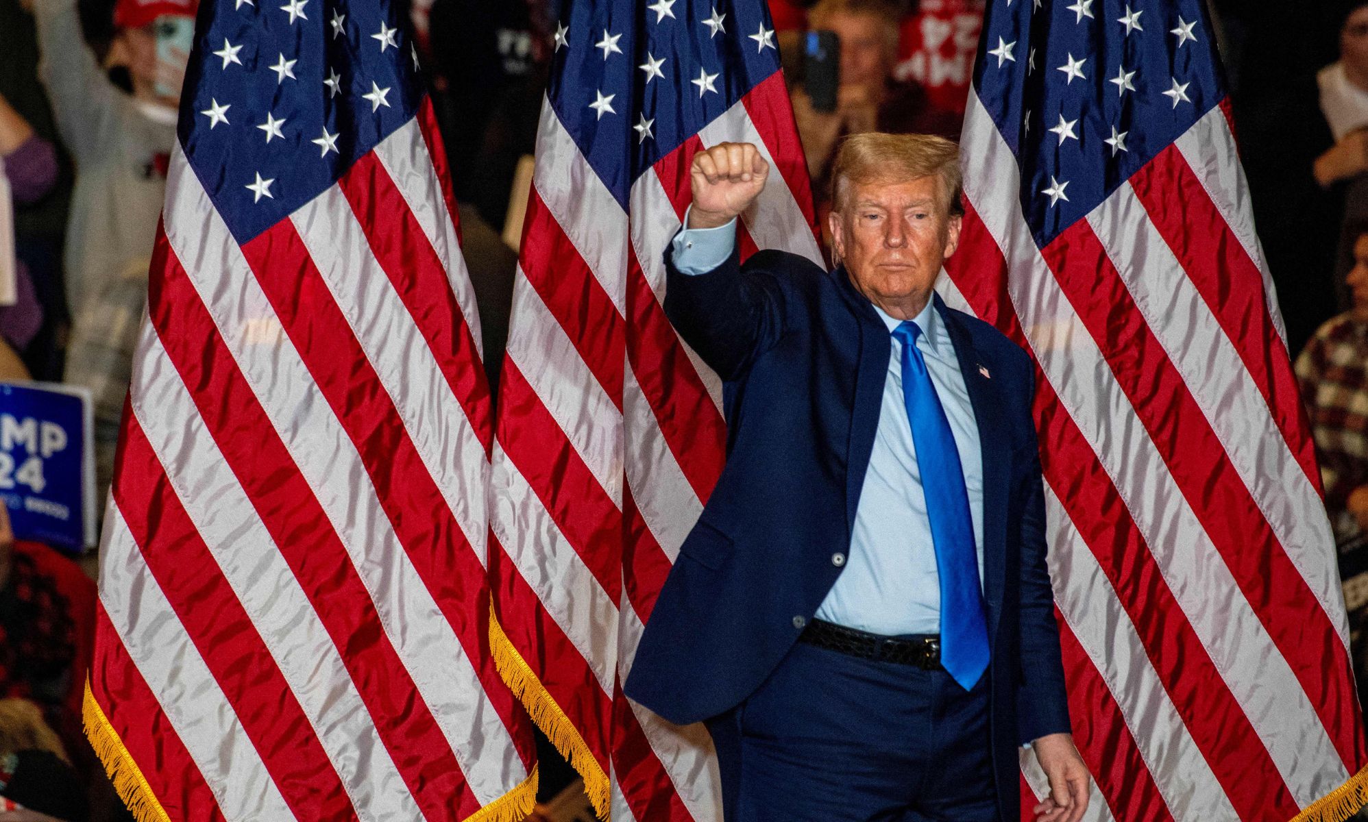 This picture shows Donald Trump standing against three American flags holding a raised fist to supporters.