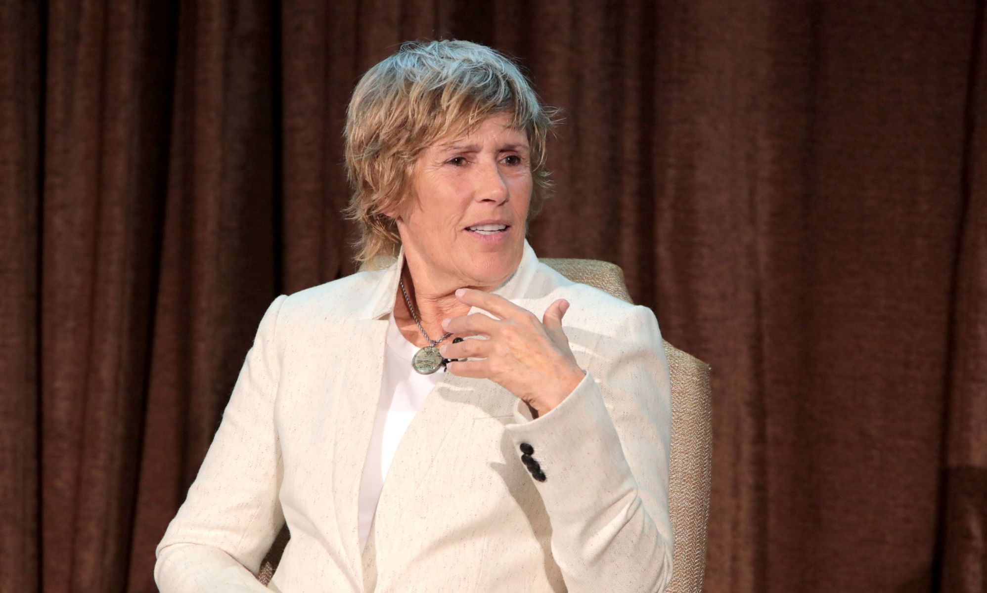 Lesbian swimmer Diana Nyad wears a cream suit while speaking on stage