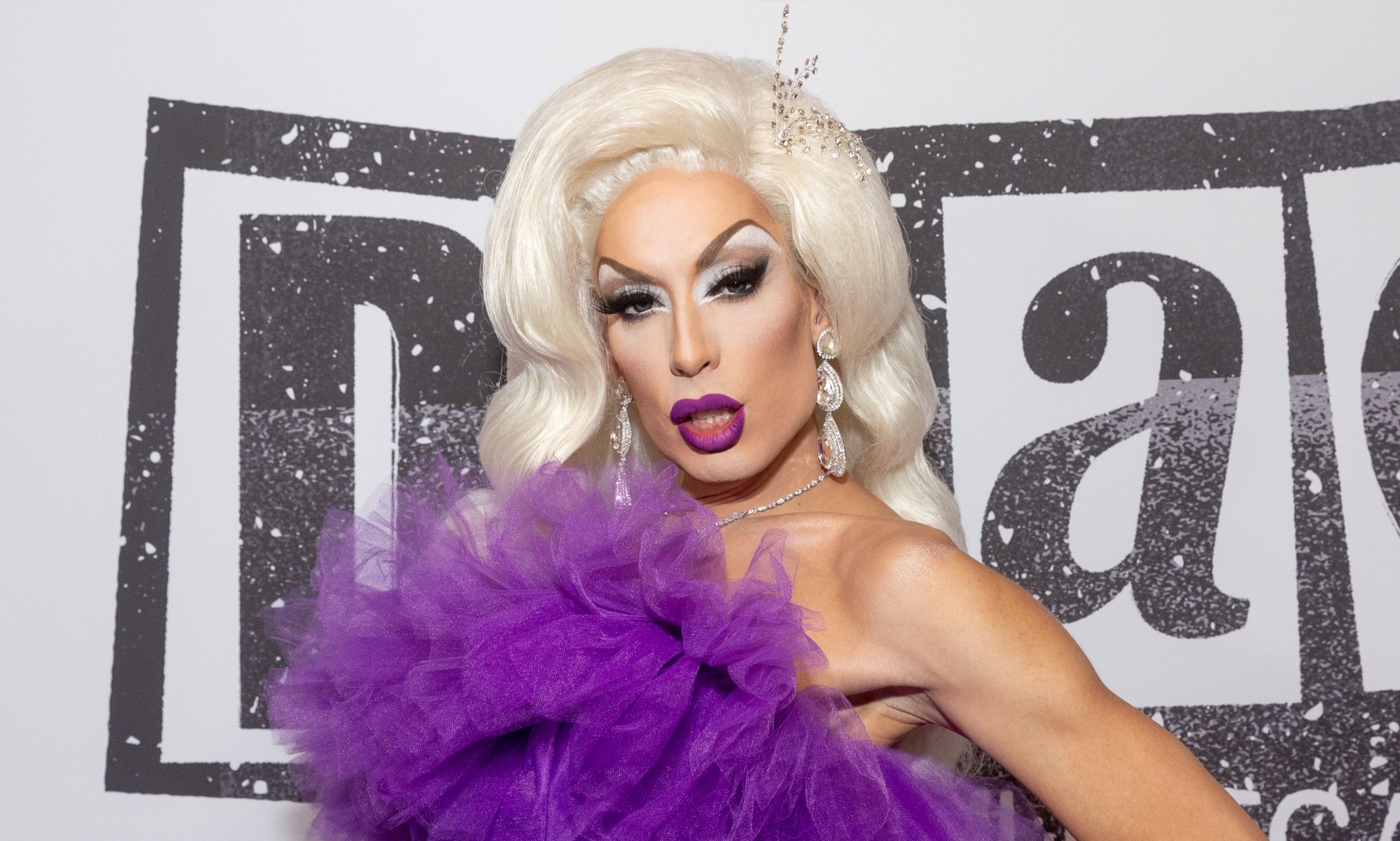 Drag Race star Alaska wears a purple dress and blonde wig.