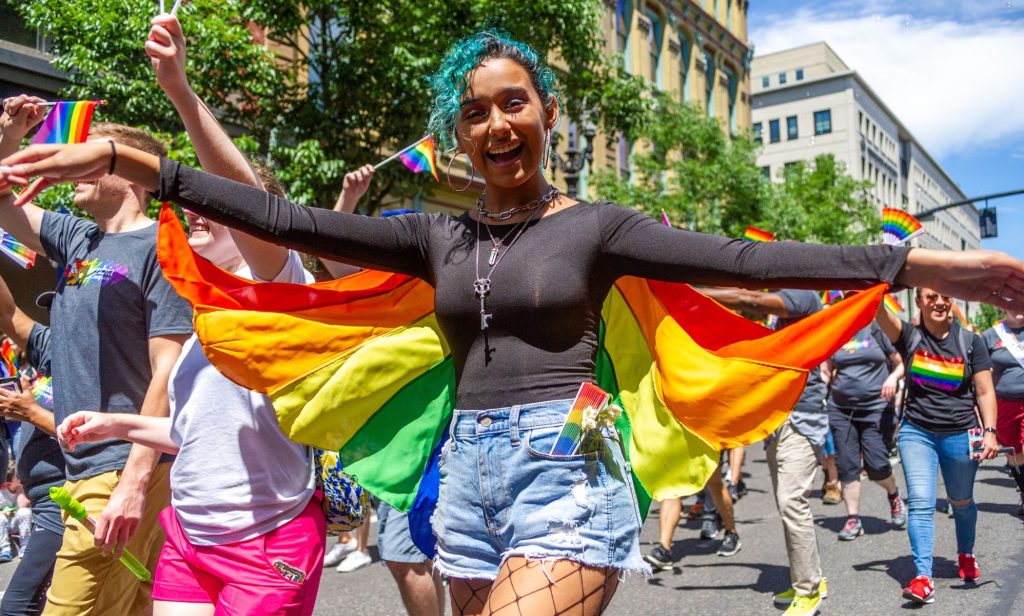 A person wears a rainbow coloured cape as they walk in an LGBTQ+ pride celebration in the US state of Oregon