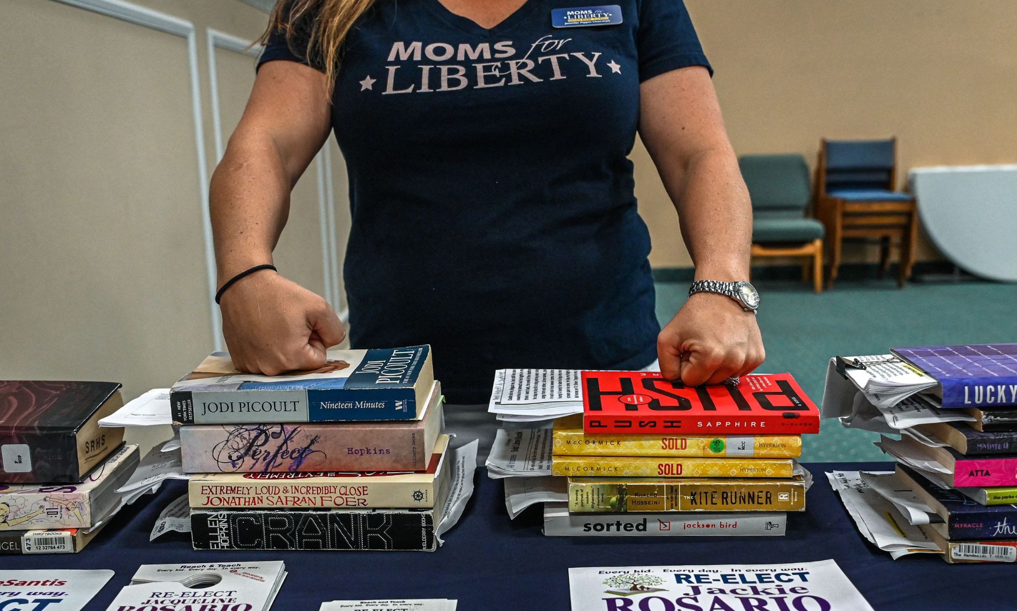 A Moms for Liberty member with her hands on two piles of books.