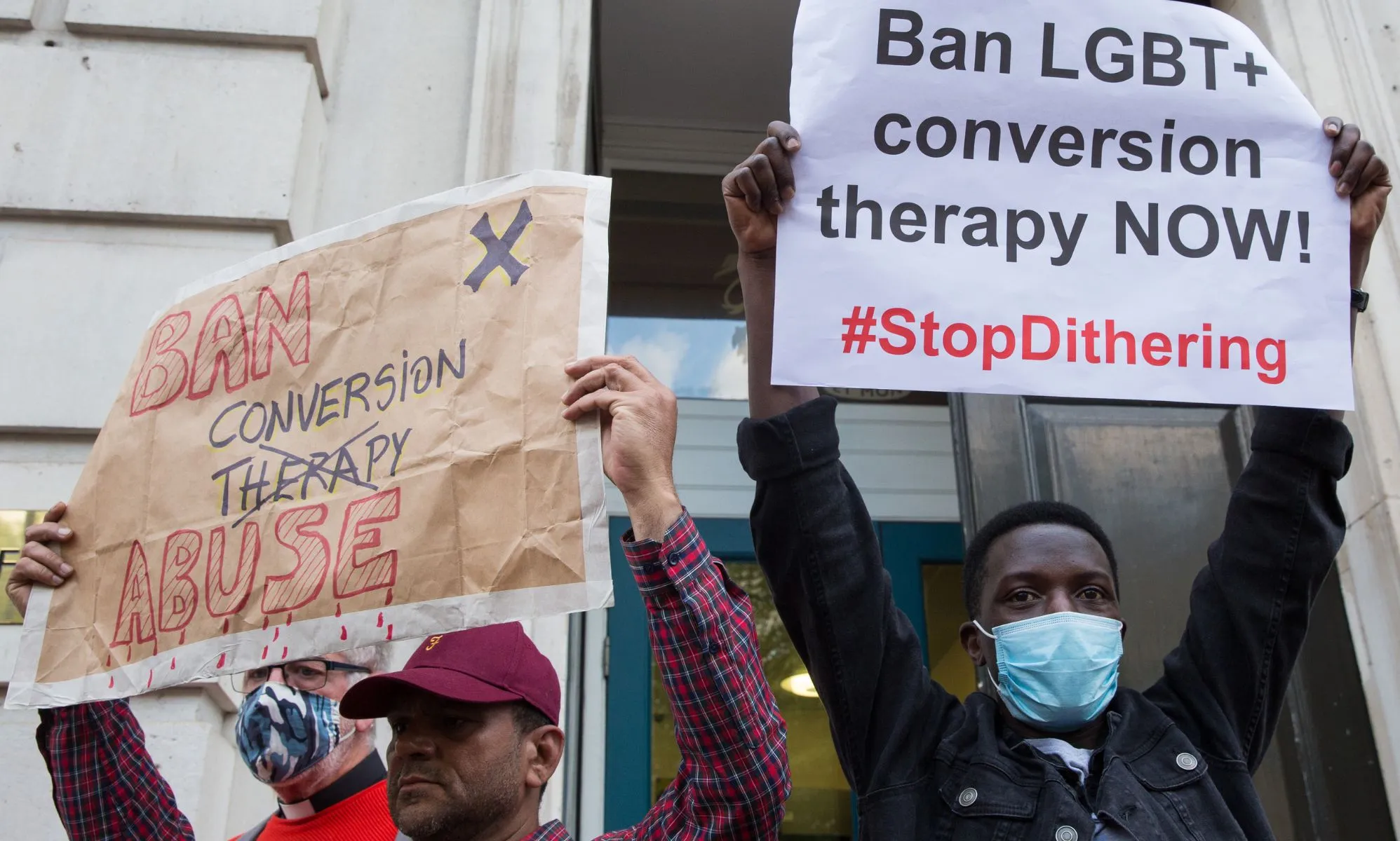 Two people stand side by side and hold up signs during an LGBTQ+ rights protest to ban conversion therapy.